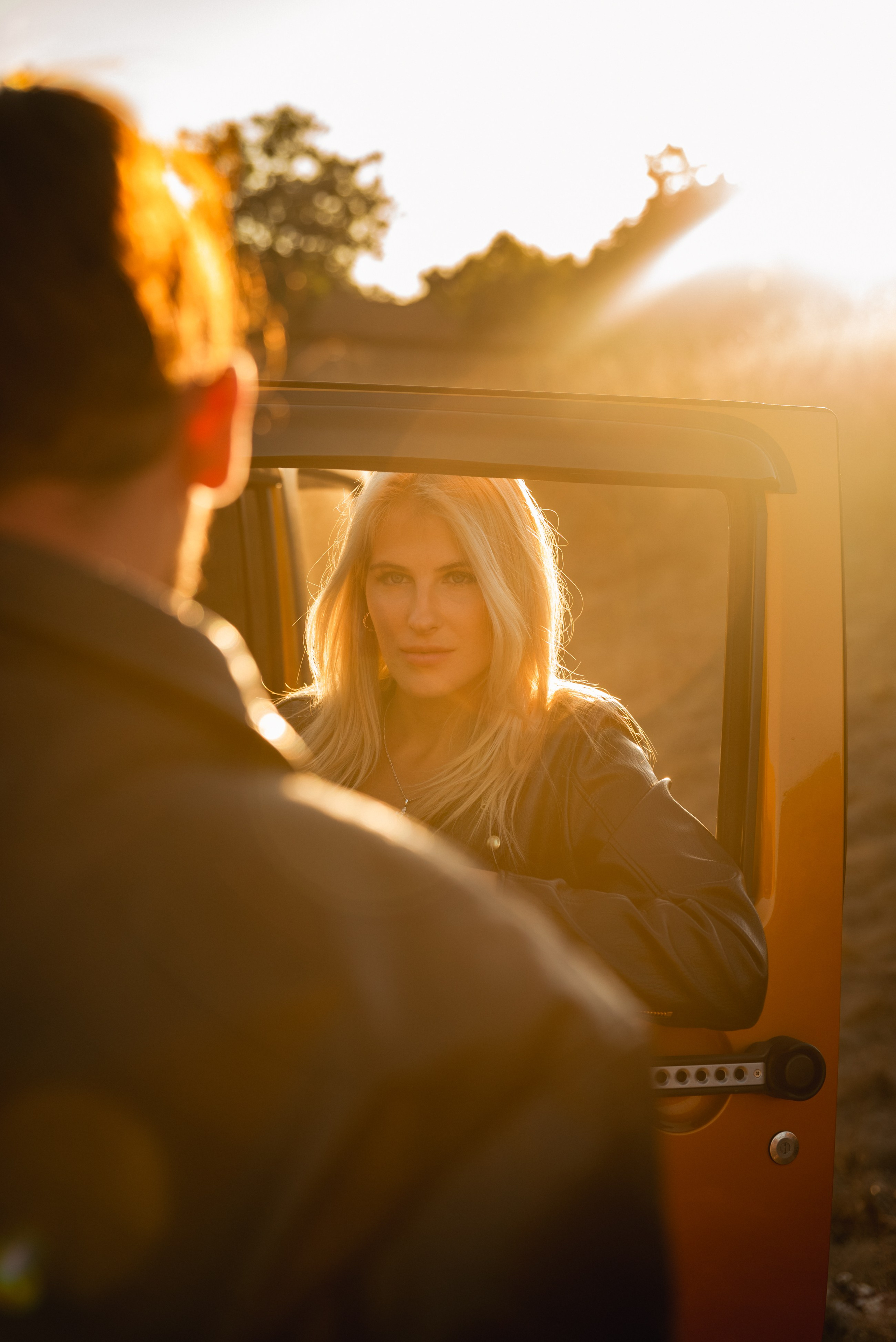 The woman flirtatiously glances at her partner through the car window, sharing affectionate anticipation.