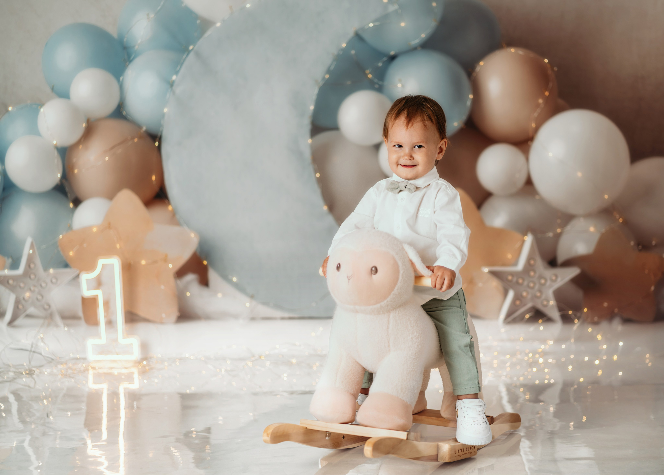 Beba na ljuljaški u obliku ovce tokom cake smash slikanja prvog rođendana u plavoj temi