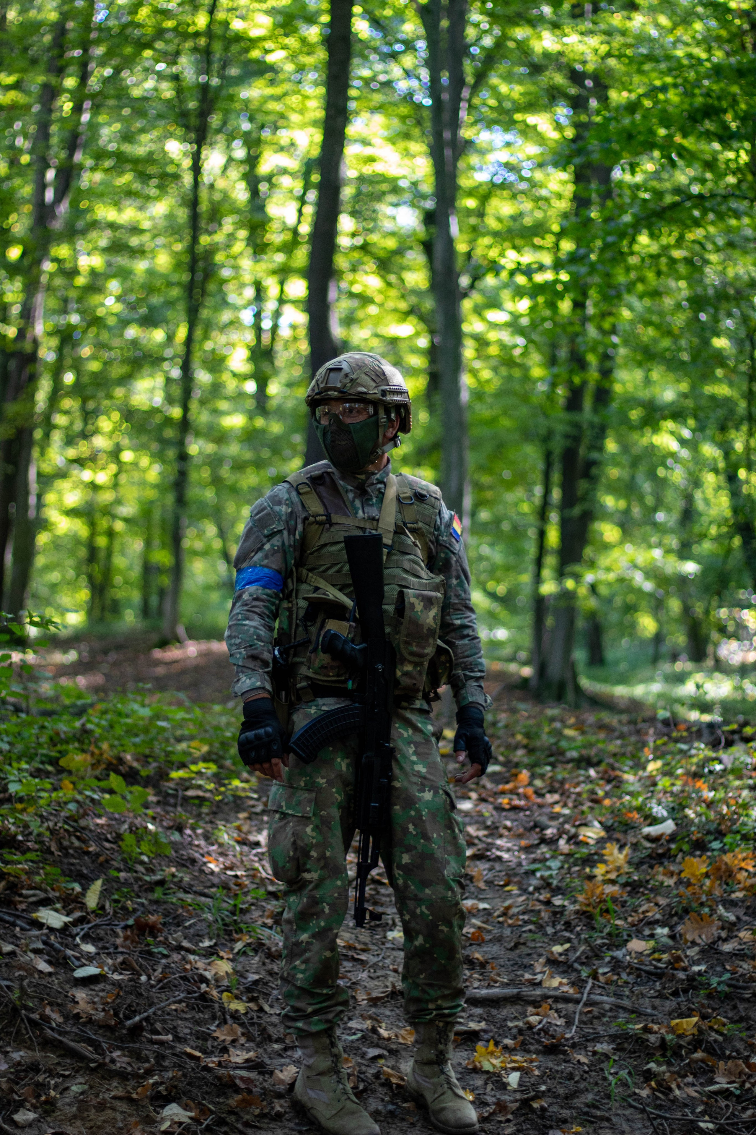 Camouflaged person standing in a dense green forest during daytime.