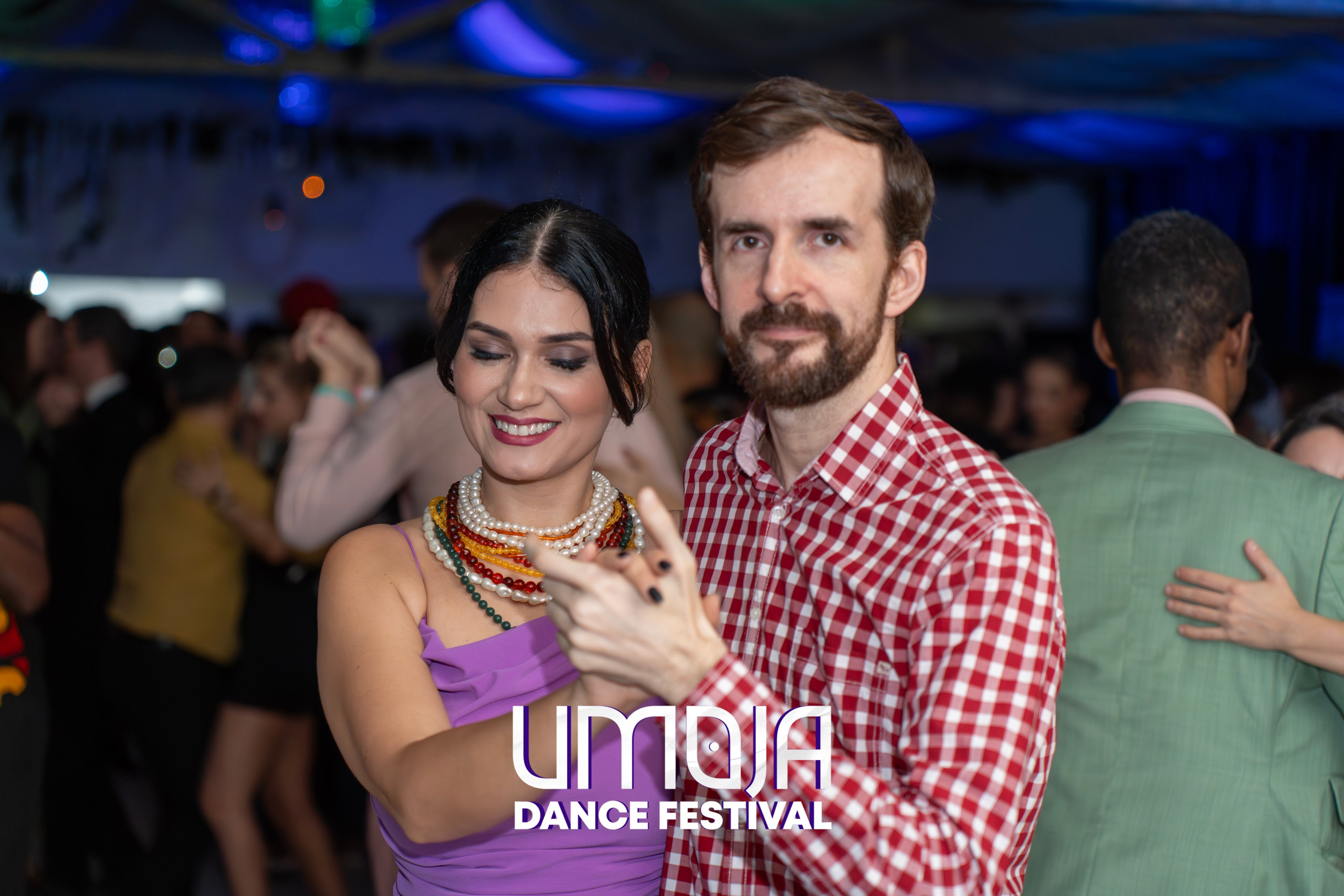 Man and woman dancing at a crowded dance festival with other couples in background.