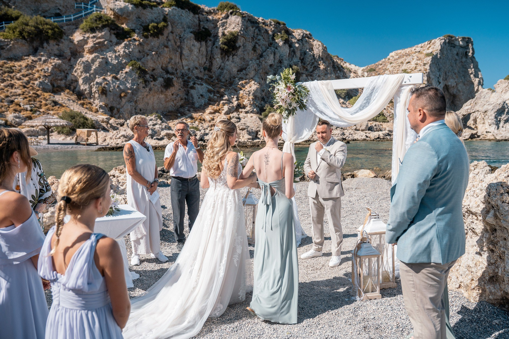 „Freie Trauung am Strand auf Rhodos mit Brautpaar, Gästen und Meerblick in Griechenland“Sie beschreibt das Bild exakt und enthält die wichtigen Suchbegriffe Trauung, Strand, Rhodos, Brautpaar und Griechenland.