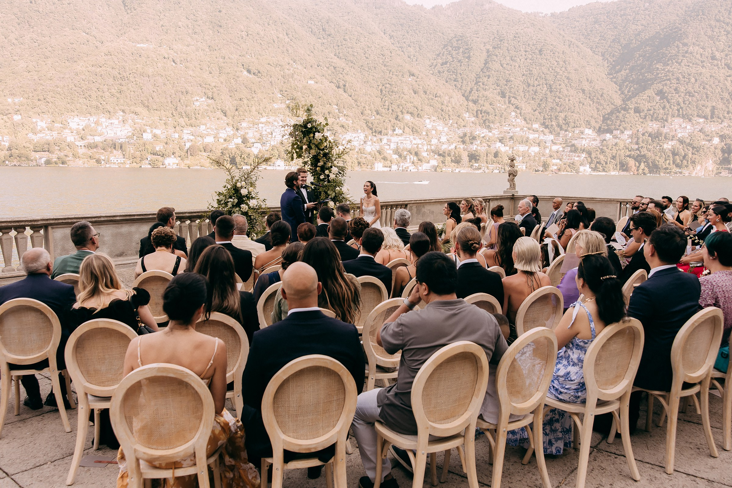 A romantic wedding ceremony taking place on the lake at a villa, with guests enjoying the scenic surroundings.