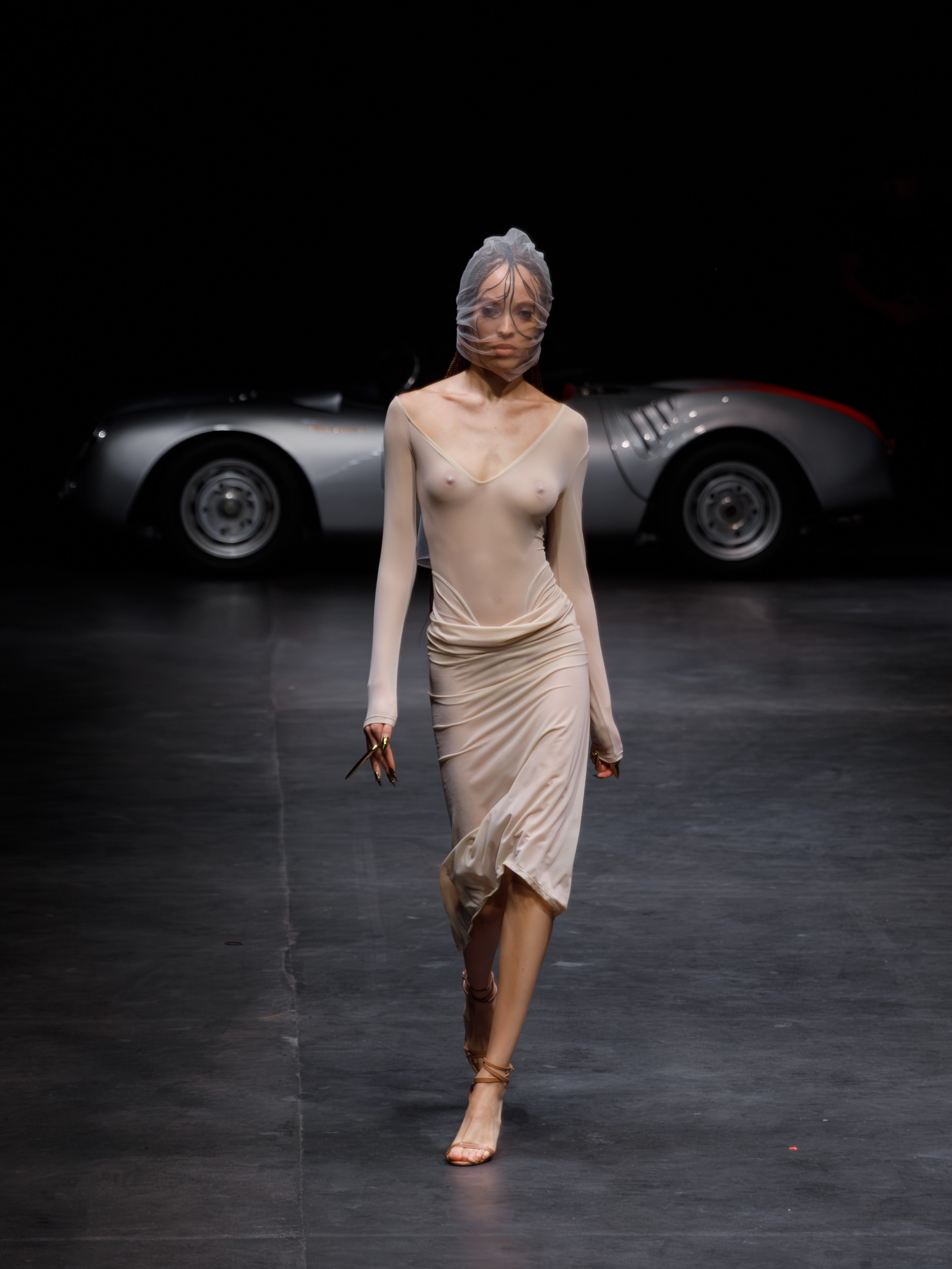 Model in nude dress standing near vintage car – editorial event photo