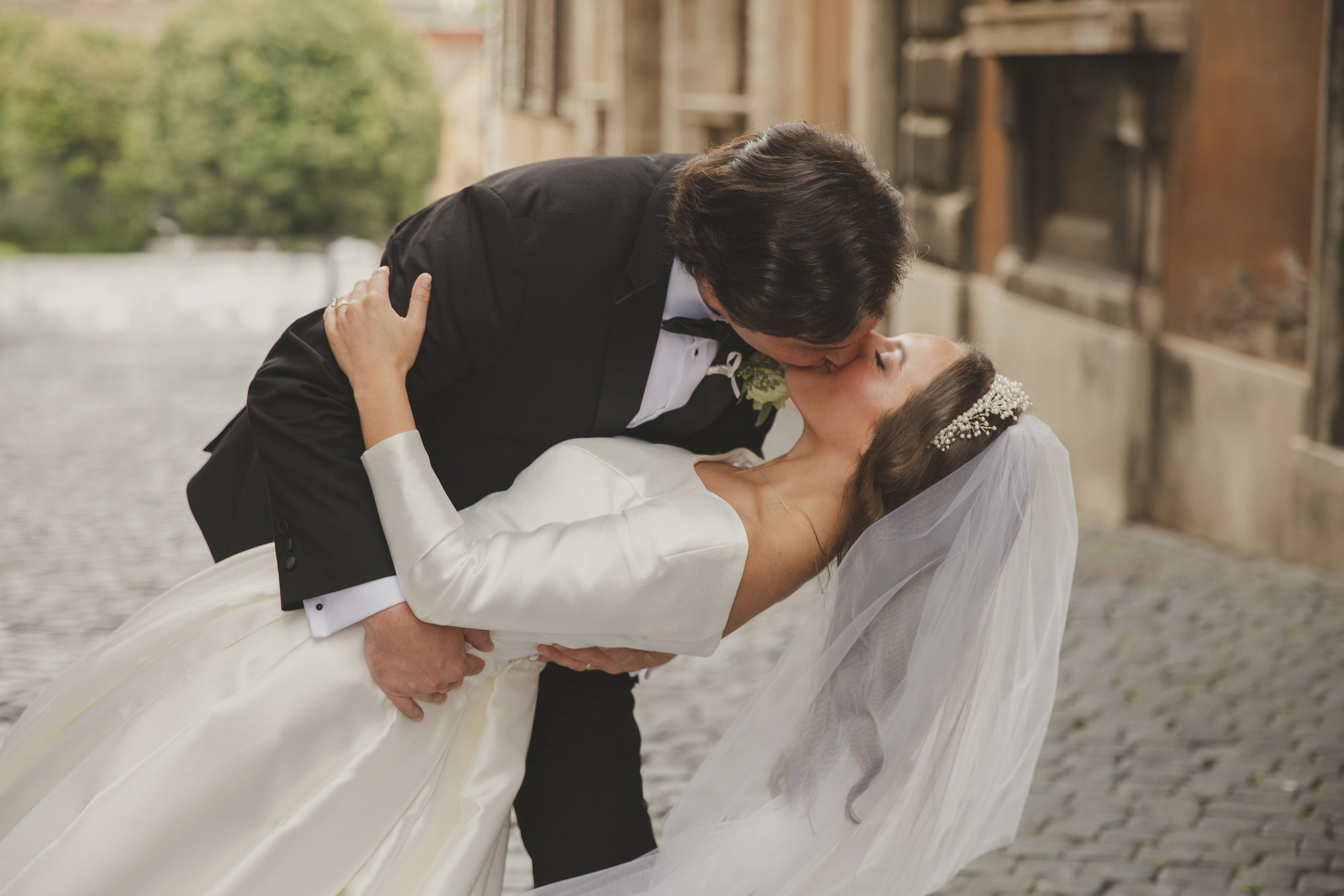 A newly married couple sharing a kiss in the streets of Rome with a stunning view of the Roman Forum.