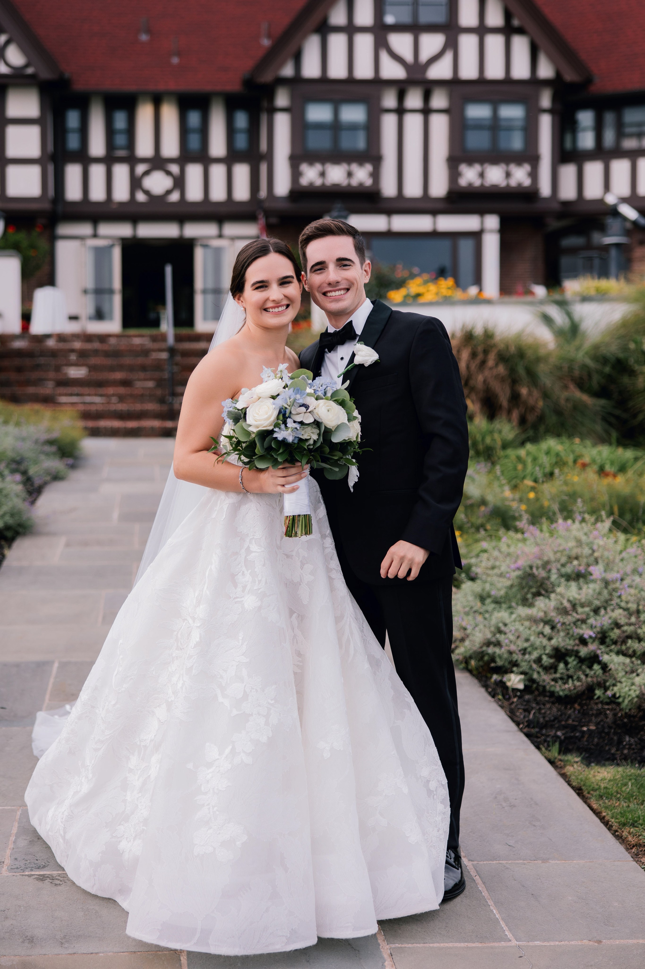 a bride and groom pose for a photo in front of a house