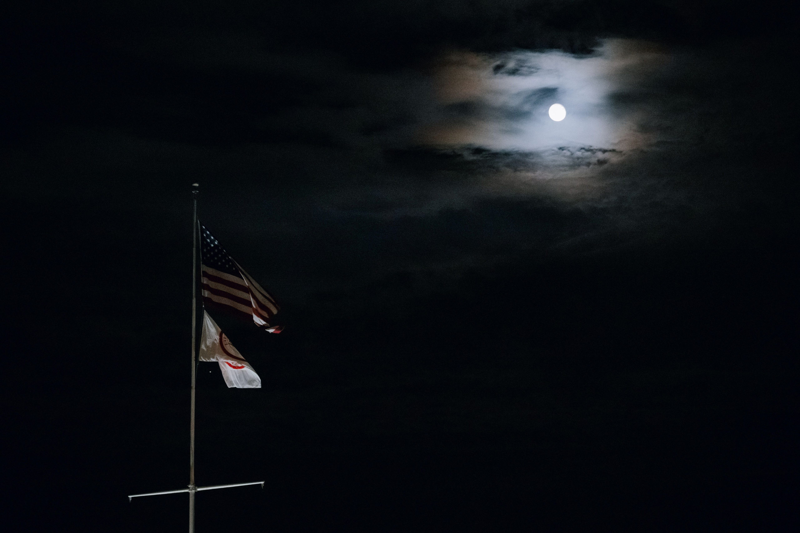 a flag flying in the dark sky with a full moon behind it