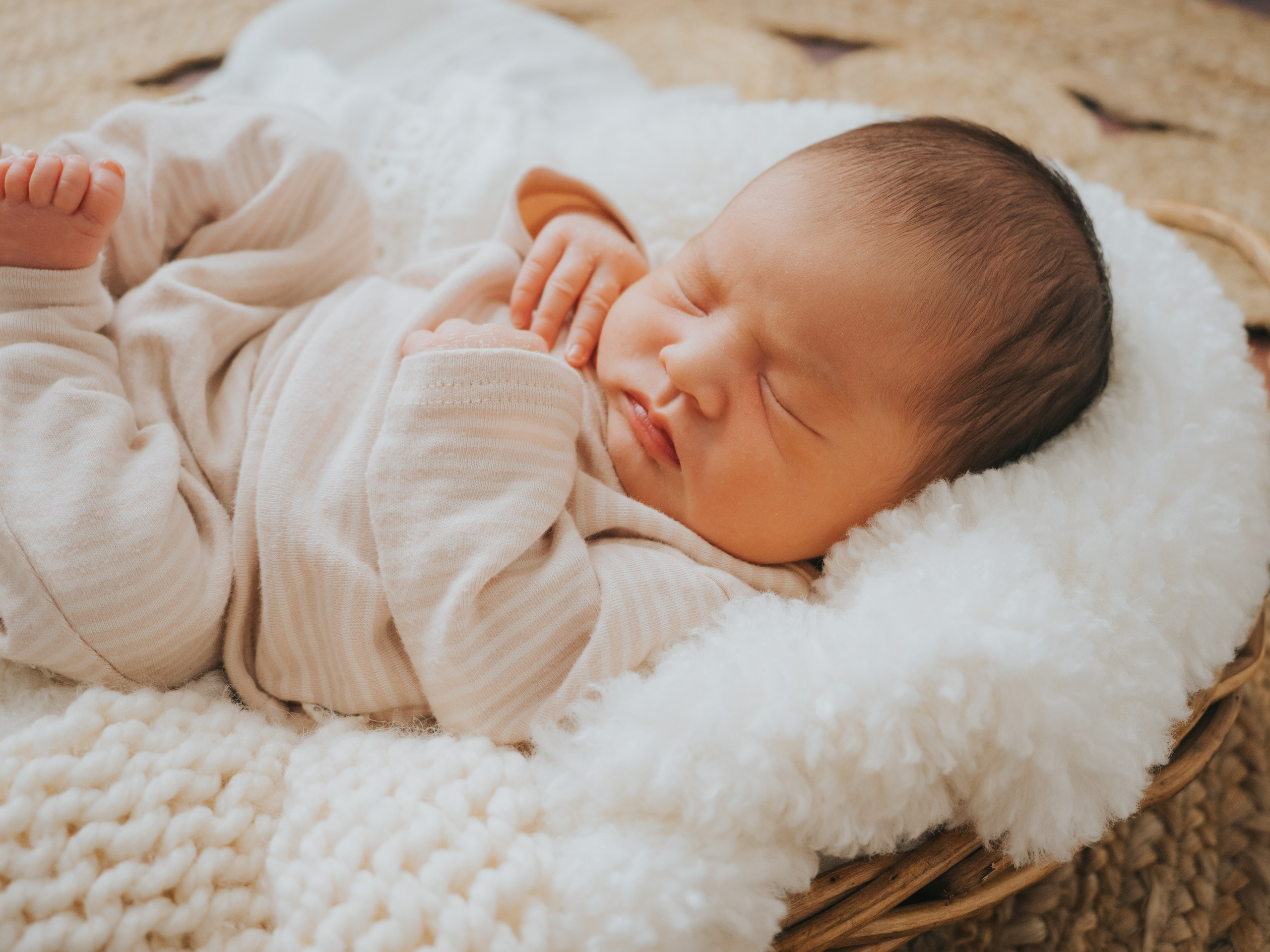 Newborn in basket surrounded by blankets with different texture.