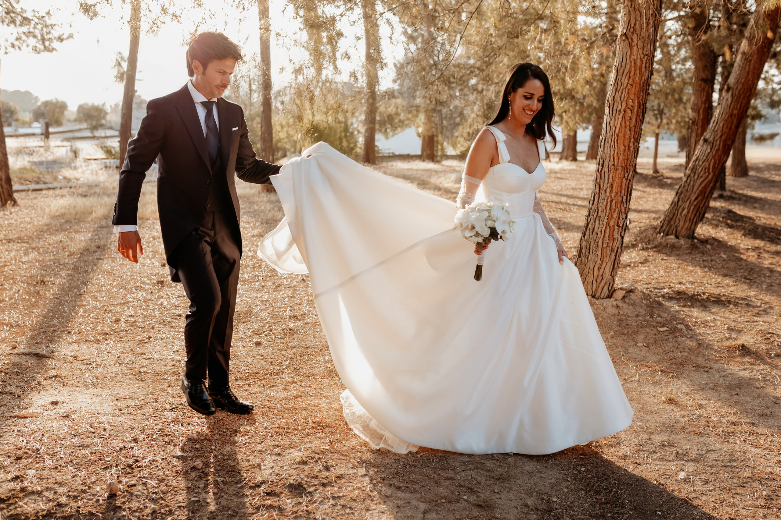 Pareja de recién casados caminando entre árboles con luz dorada, fotografía natural en exteriores