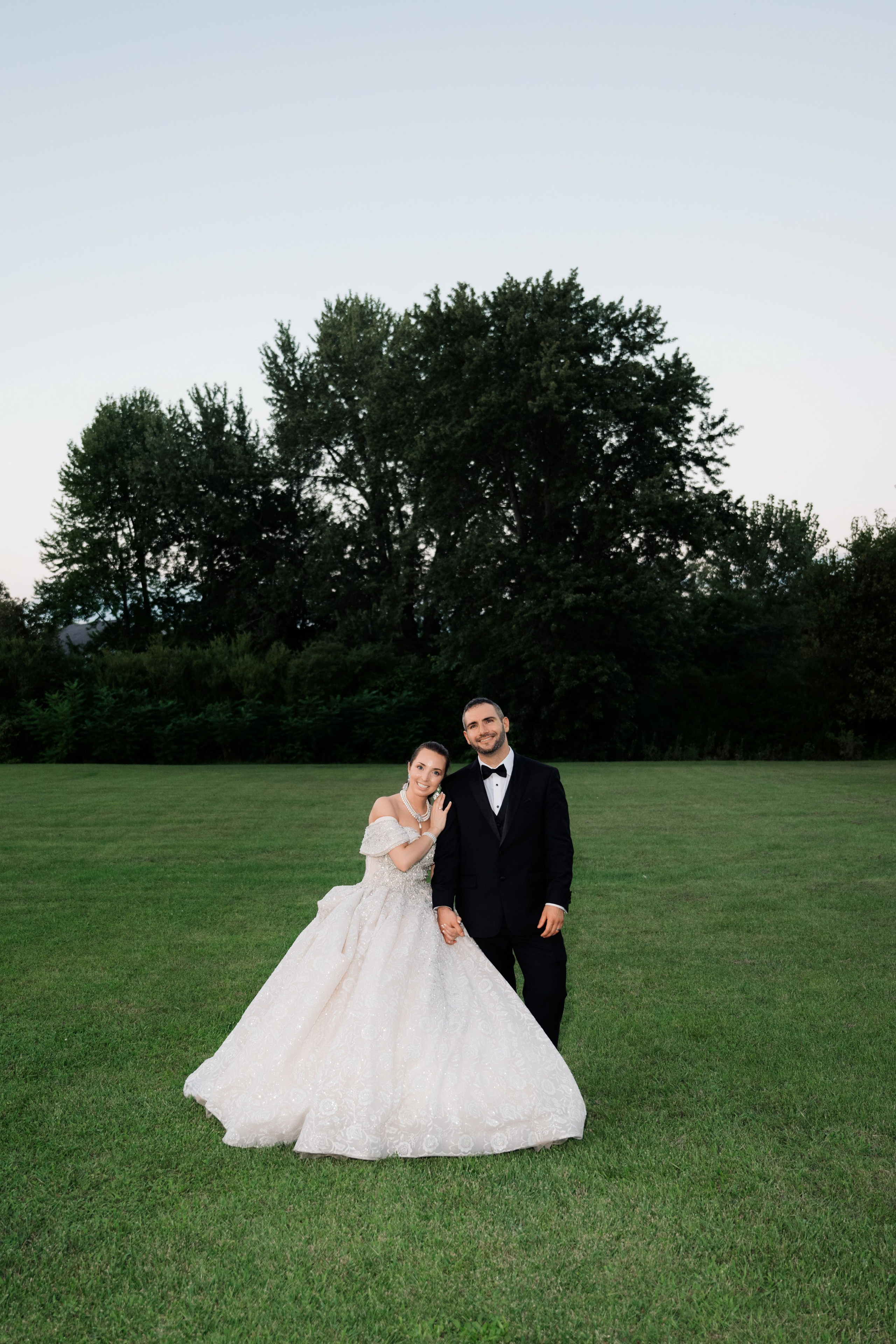 a bride and groom pose for a photo in a field