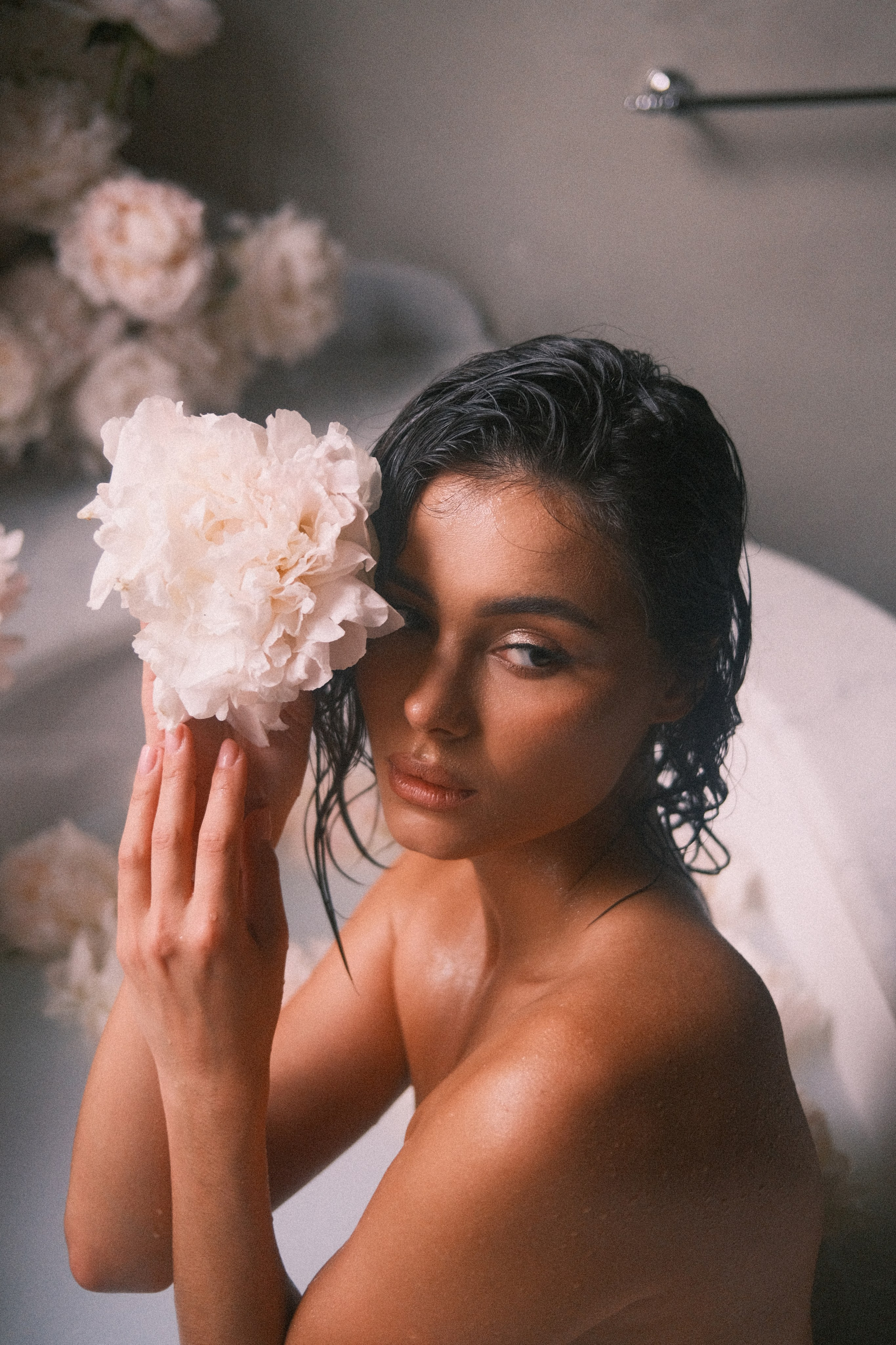 A bride tenderly holding a white peony close to her face, her wet hair and glowing skin enhancing the softness of the flower.