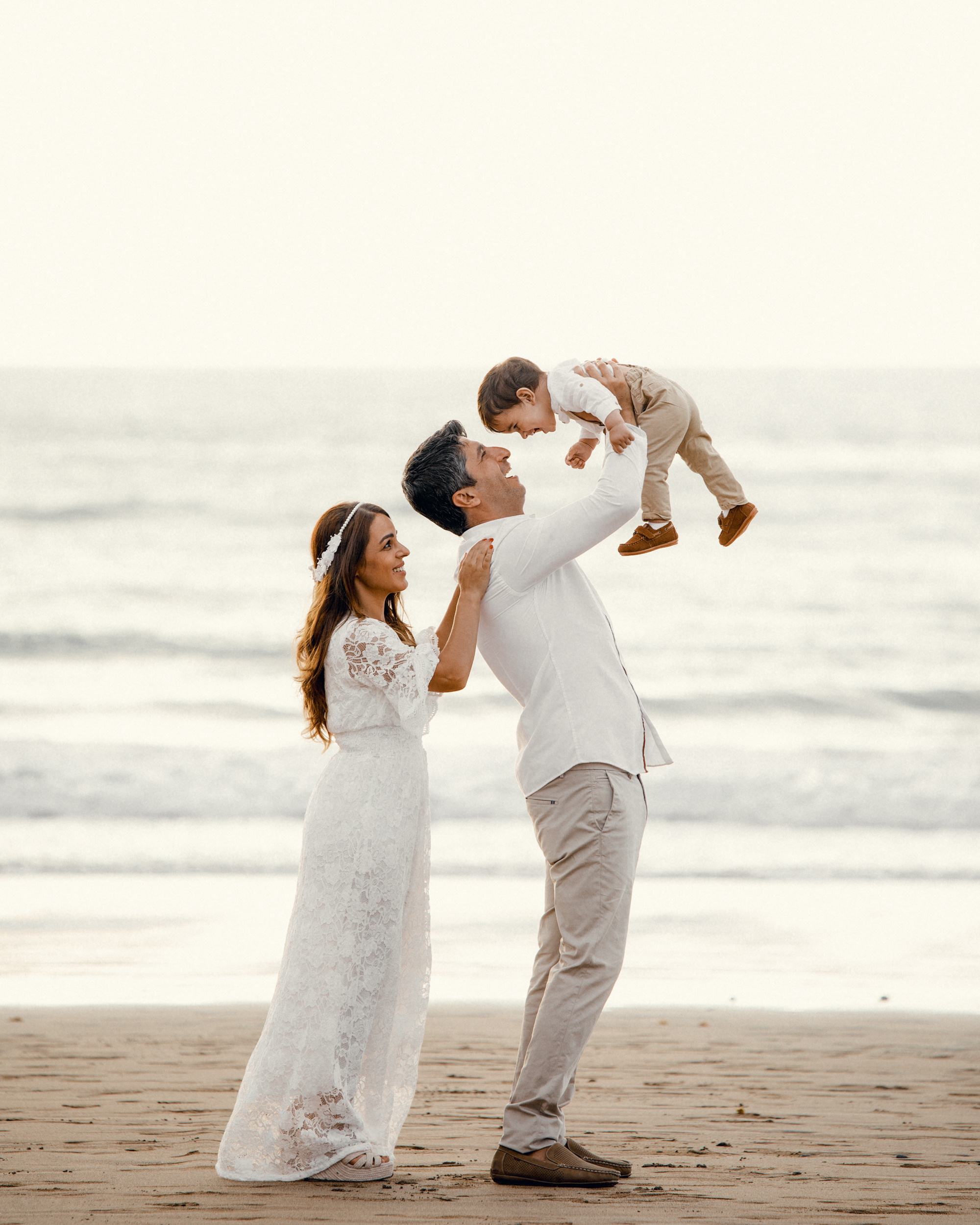 A man and woman are holding their baby on the Las Canteras beach