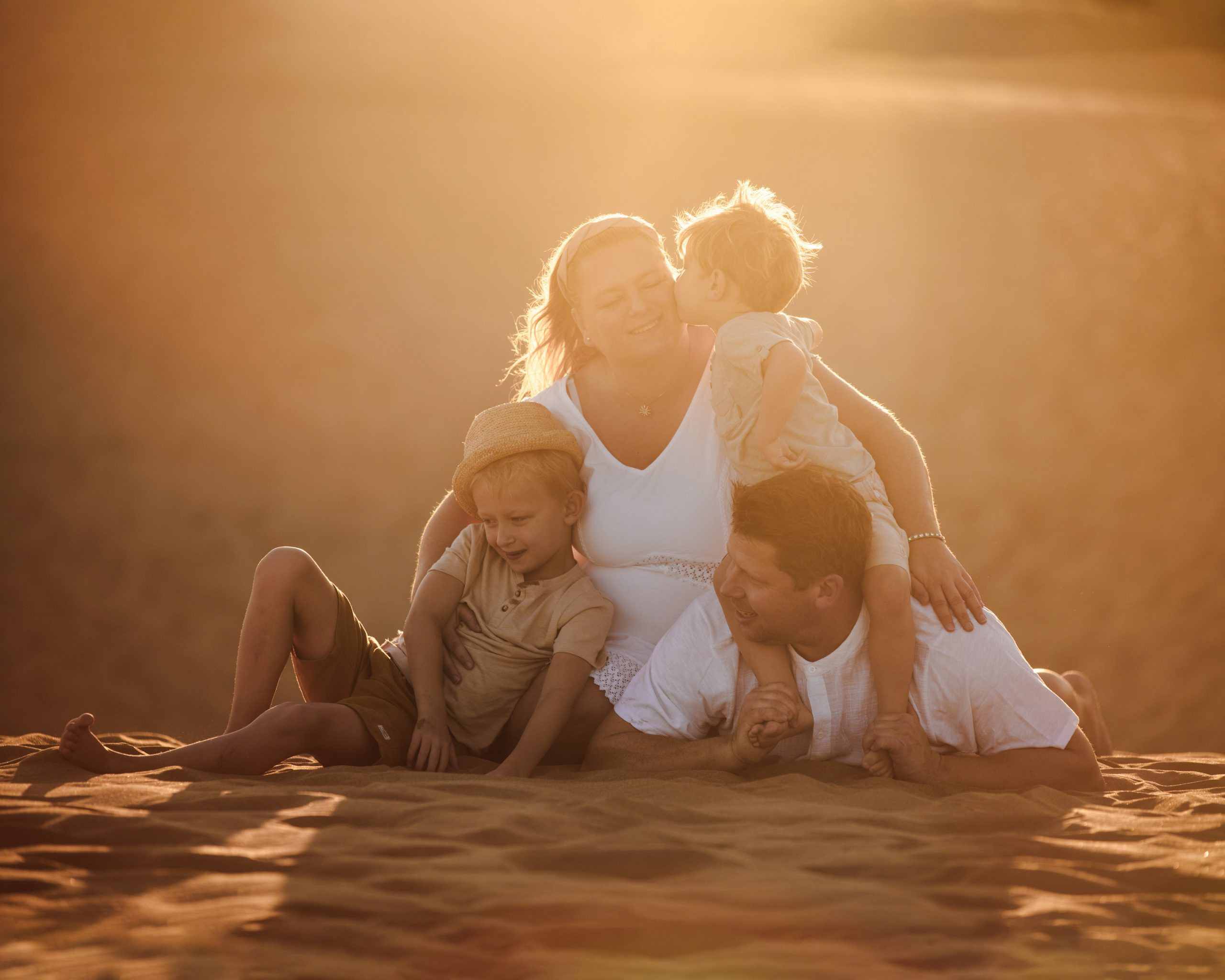 A family sits on a sand dune at sunset.