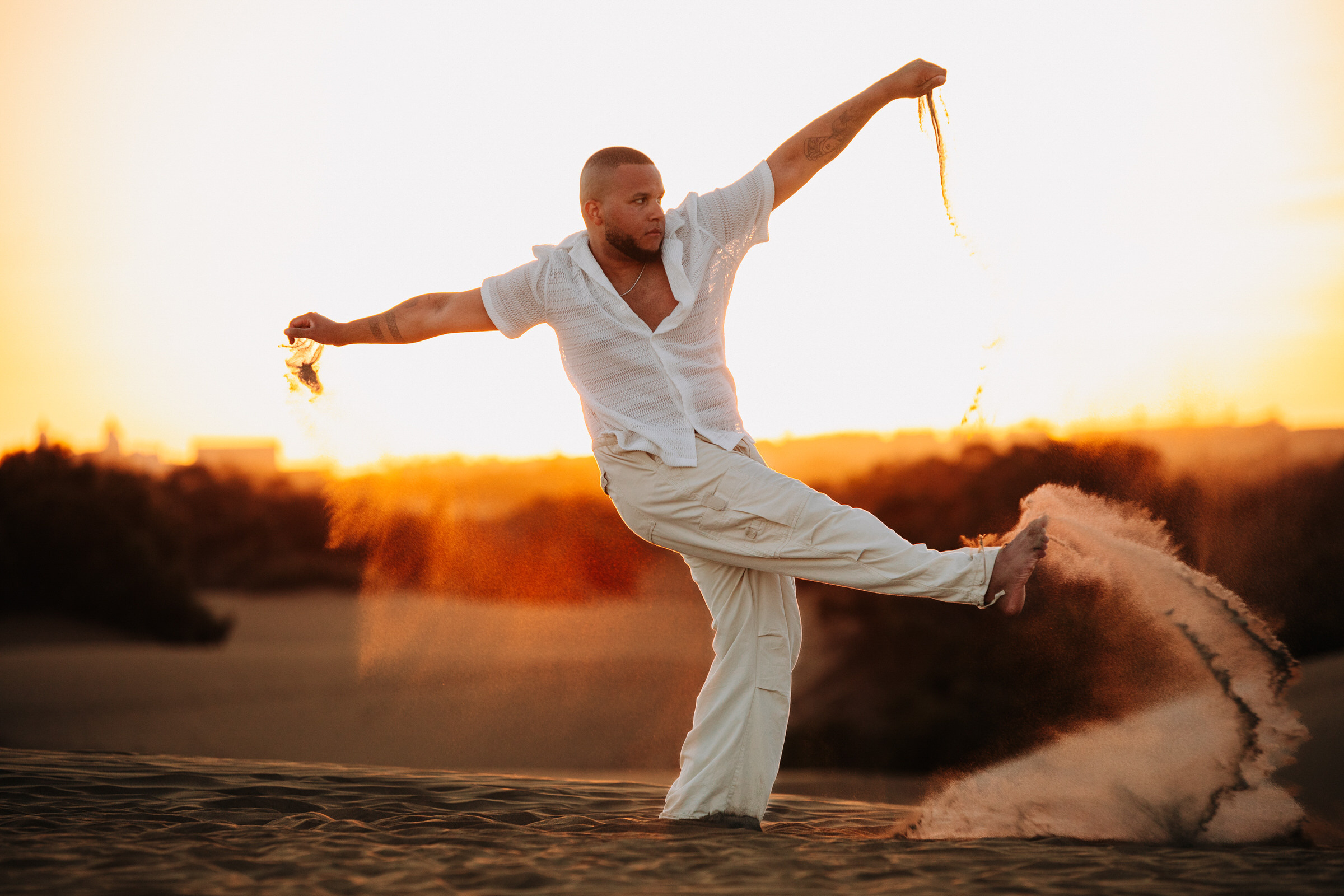 A man doing karate in the sand at sunset.