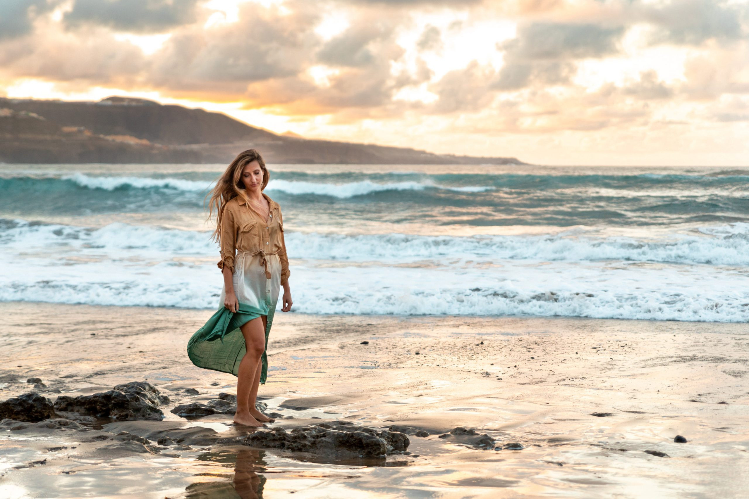 A woman standing on the beach at sunset.