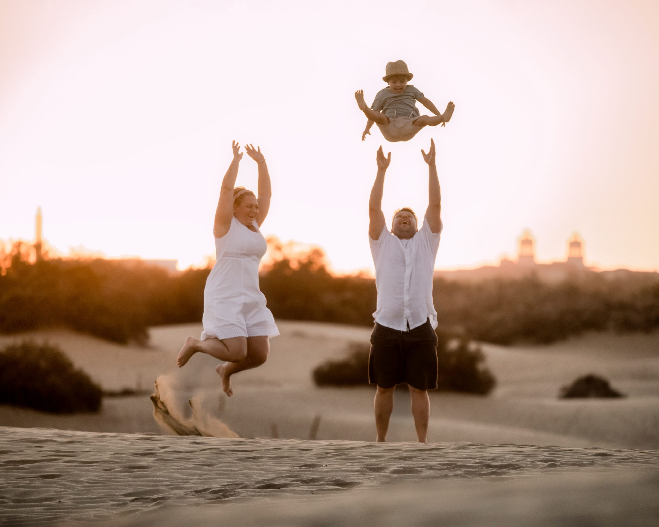 A family is holding their child in the air in the sand dunes.