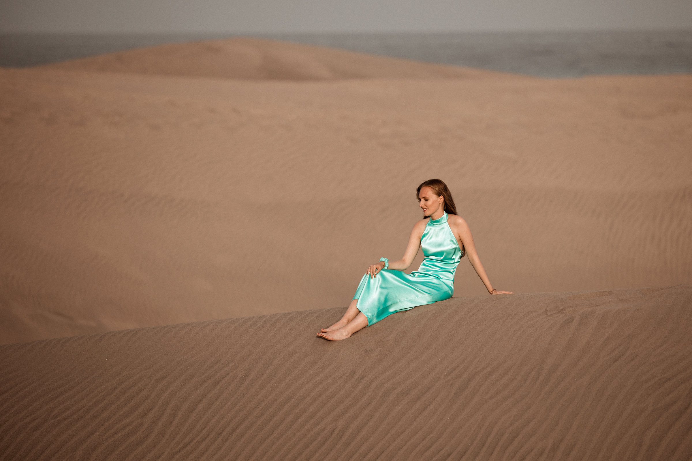 A woman in a blue dress sitting on a sand dune.