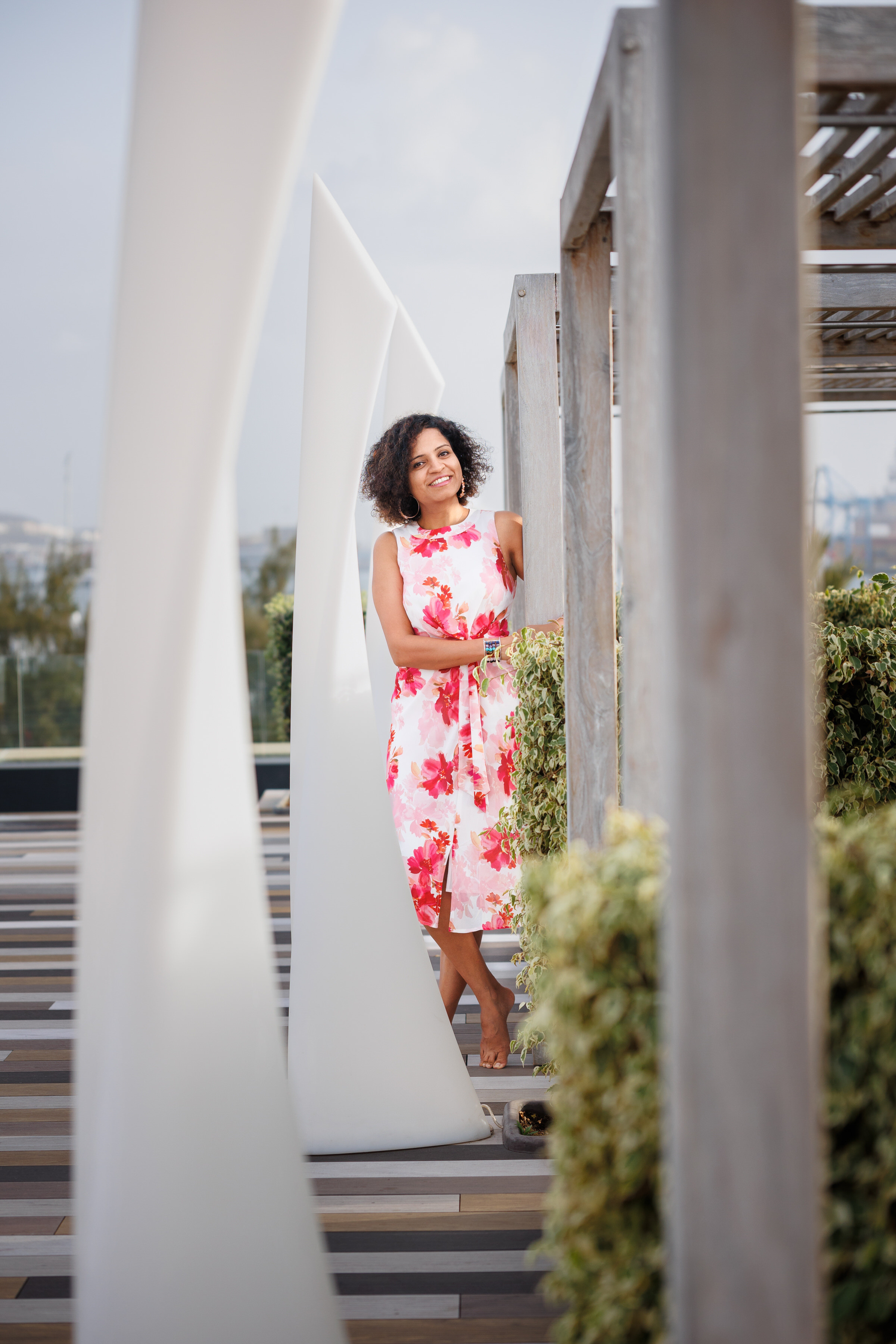 A woman in a floral dress leaning against a wooden structure.