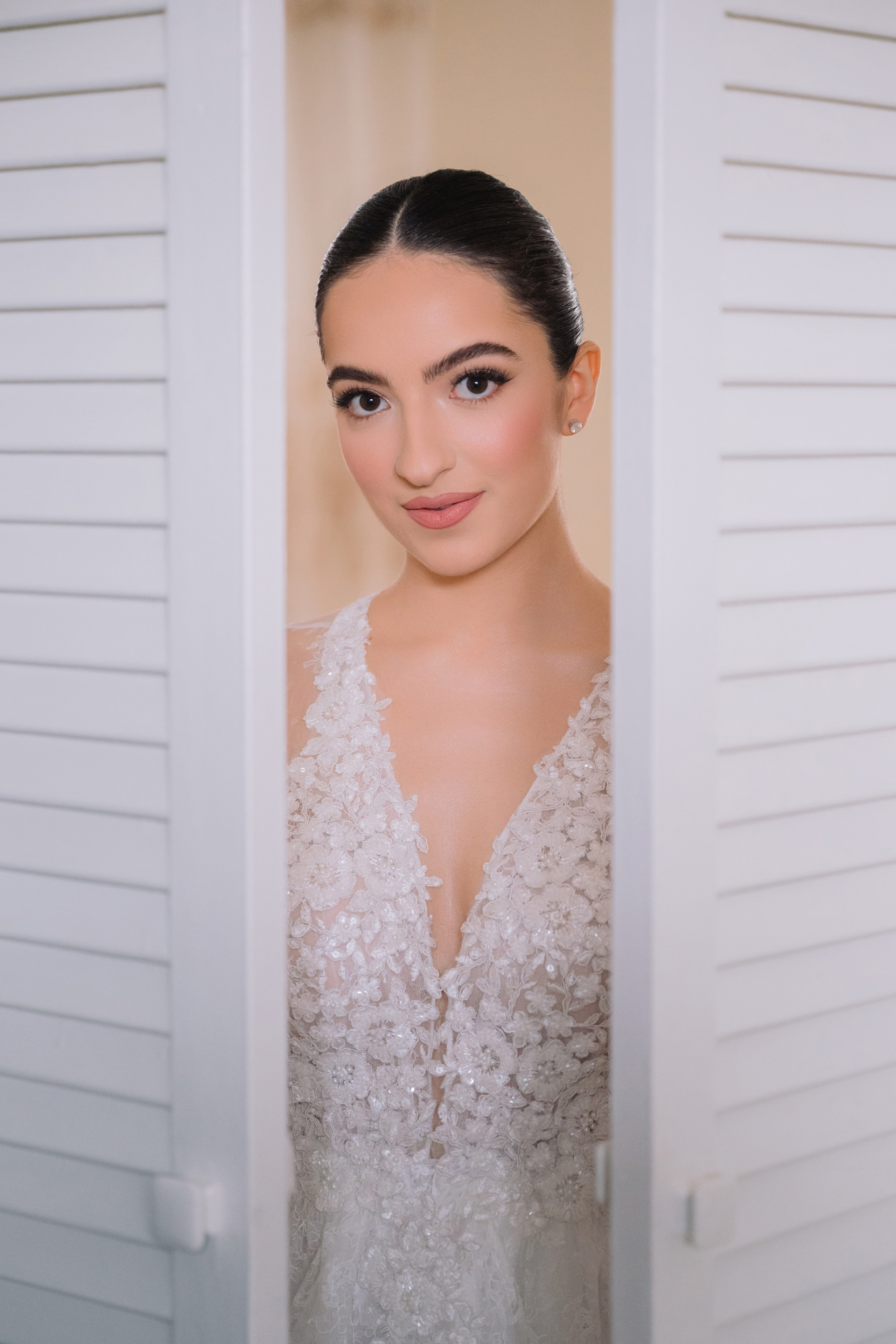 a bride looking through the shutters of her wedding dress