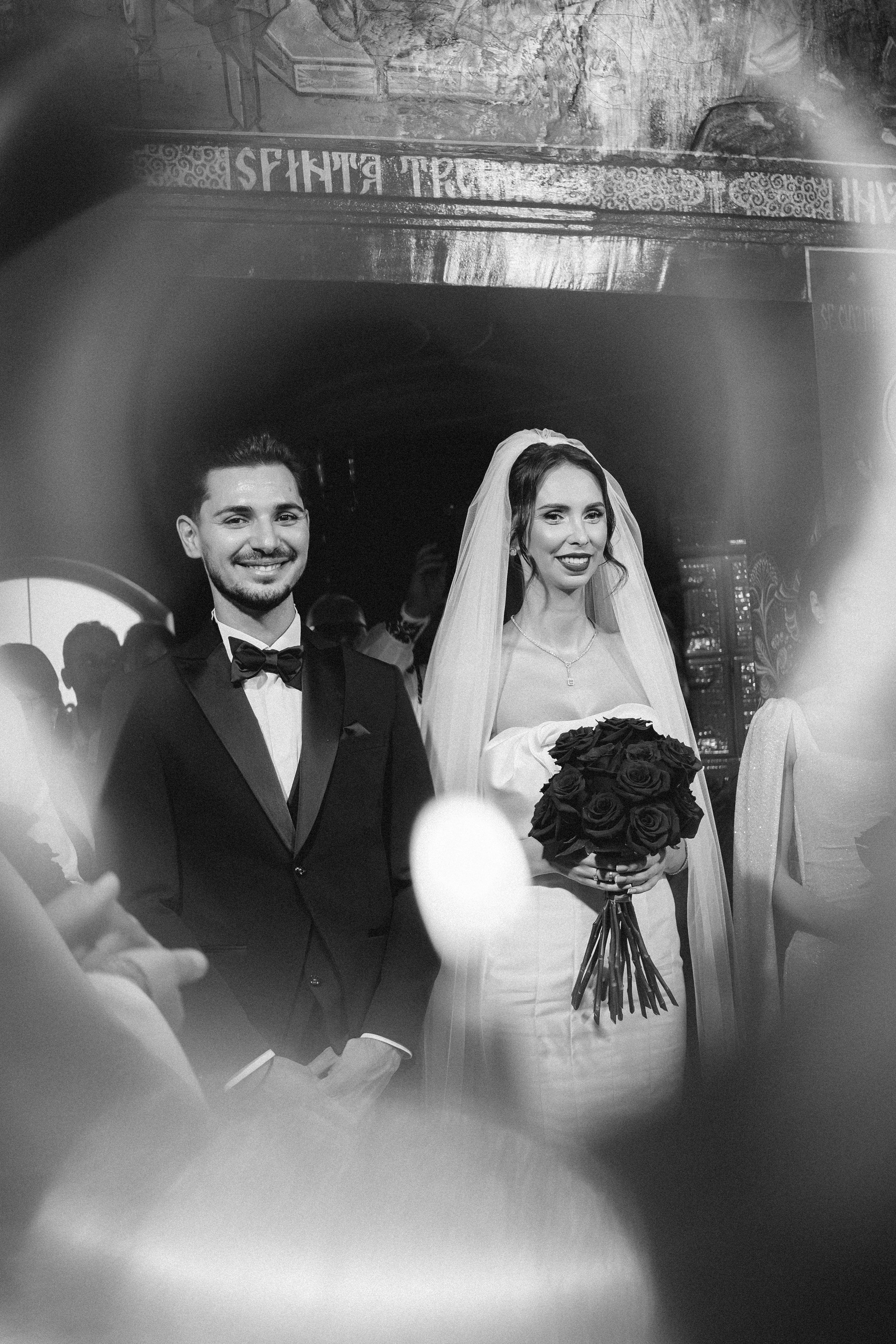 Cadru artistic alb-negru cu mirii în timpul ceremoniei religioase.