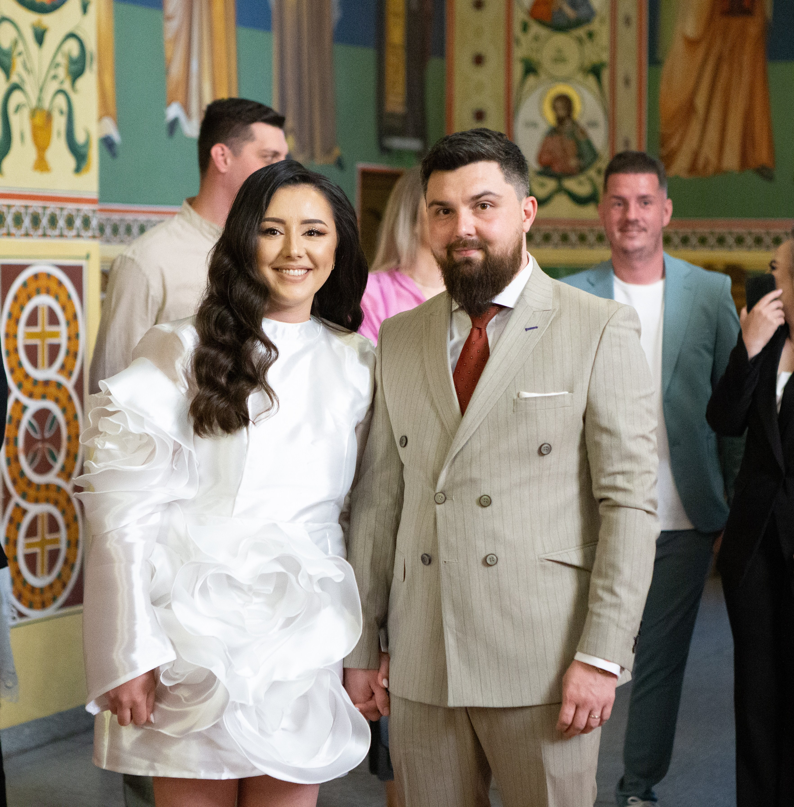 Couple holding hands inside church with colorful religious murals in the background.