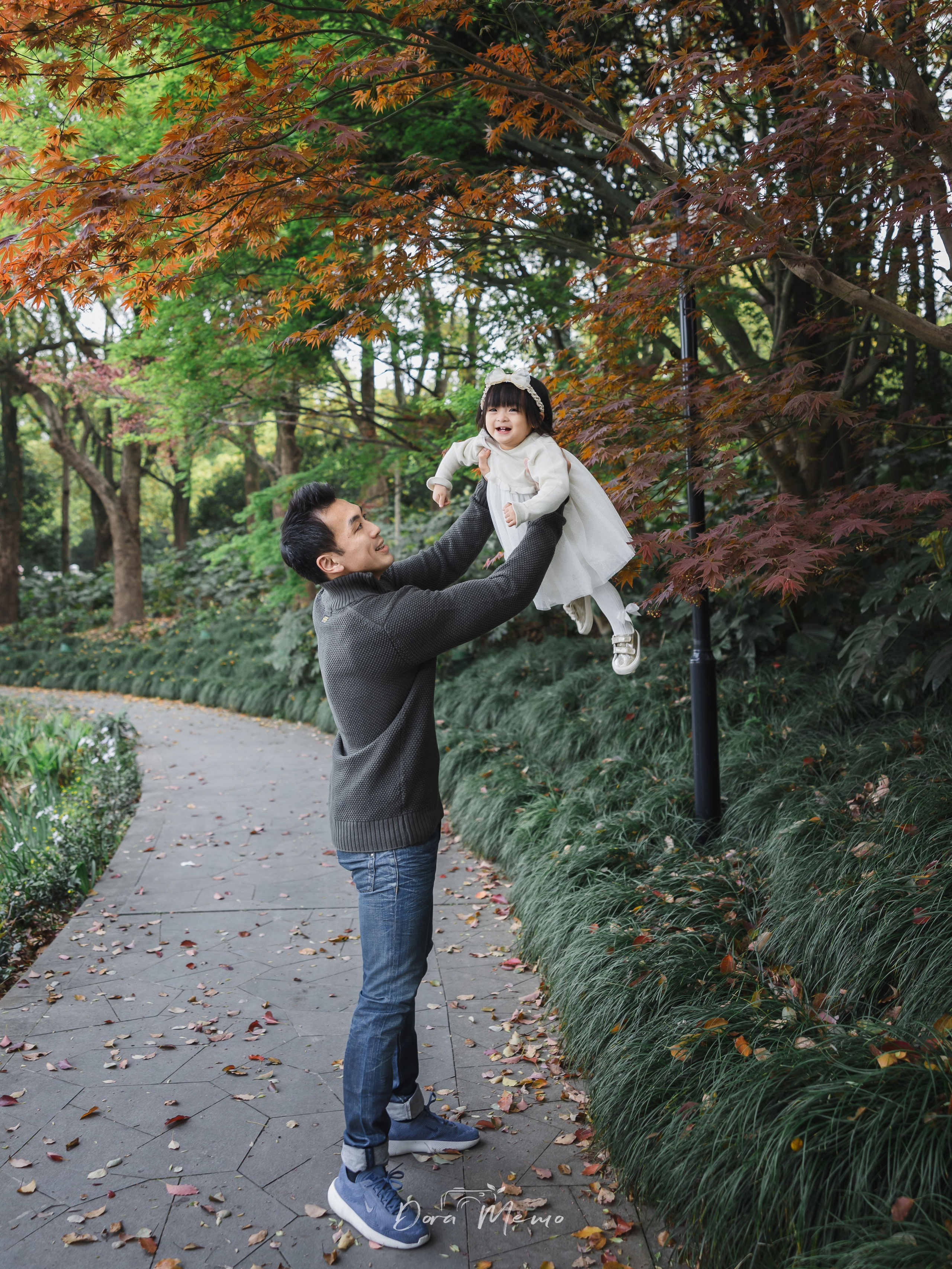 A father lifts his toddler daughter against a backdrop of autumn red leaves in Shanghai