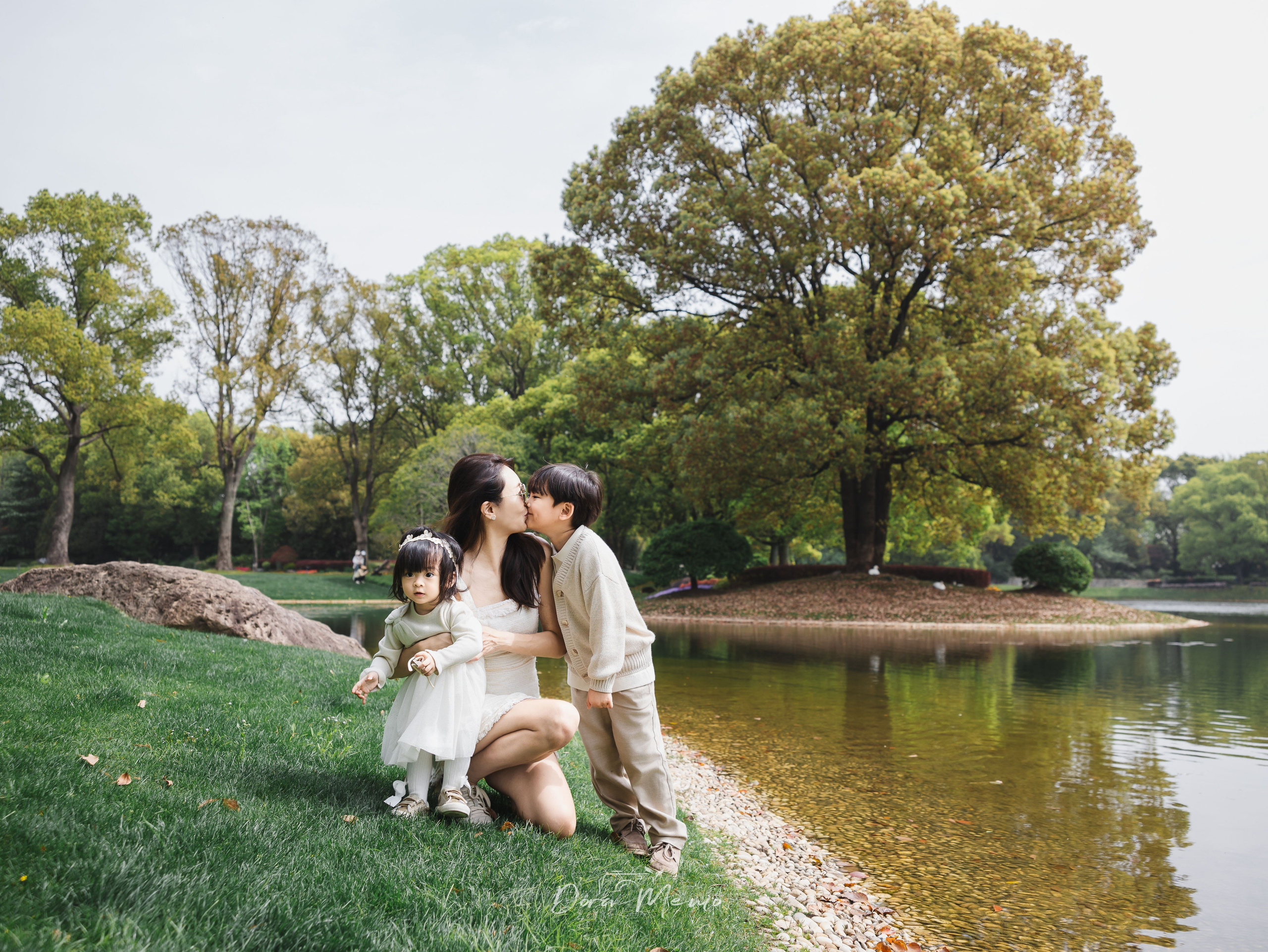 A mother crouches on the grass hugging both her children, the boy leaning in to kiss her cheek