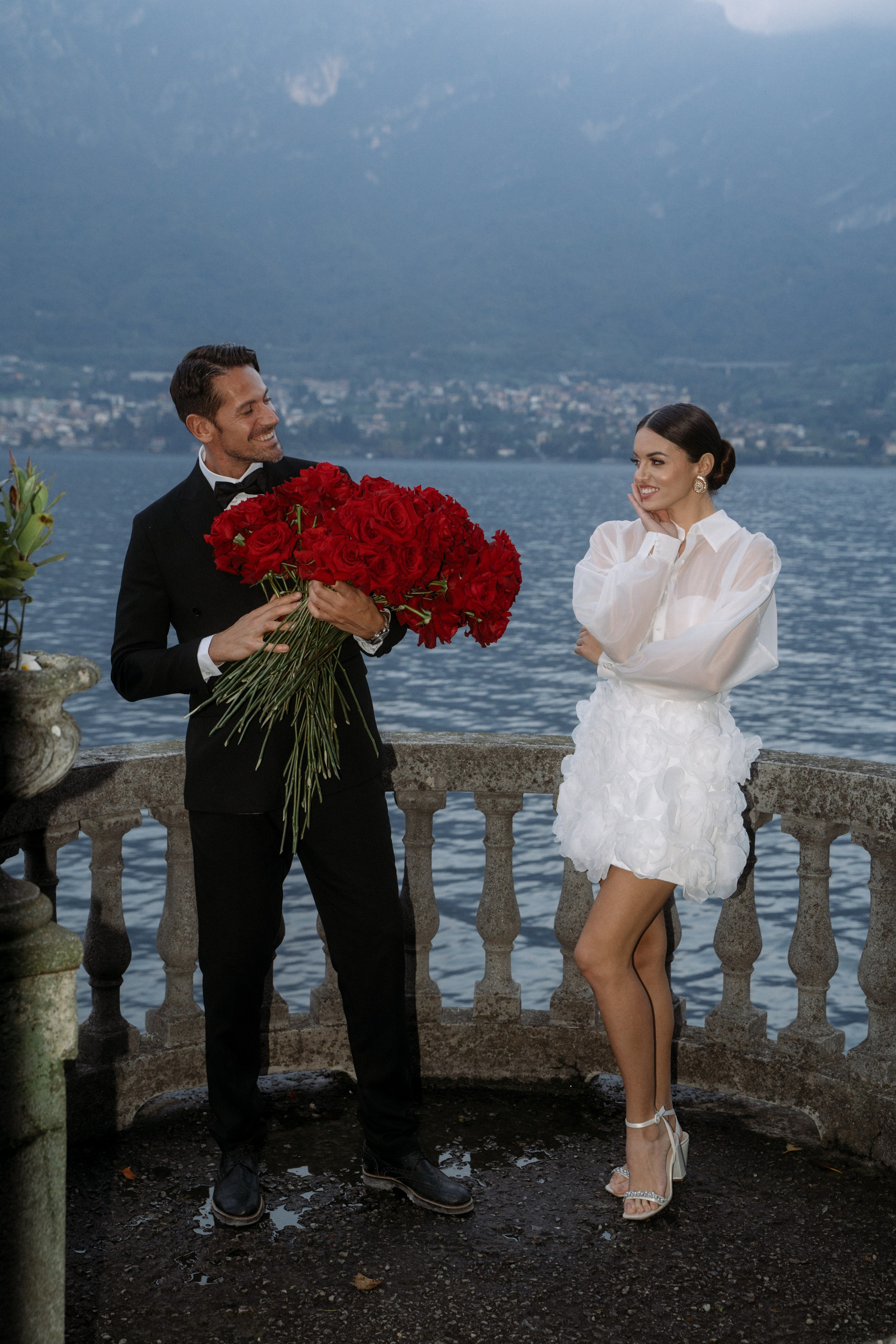 Wedding on Lake Como, with the groom presenting a large rose bouquet to his bride