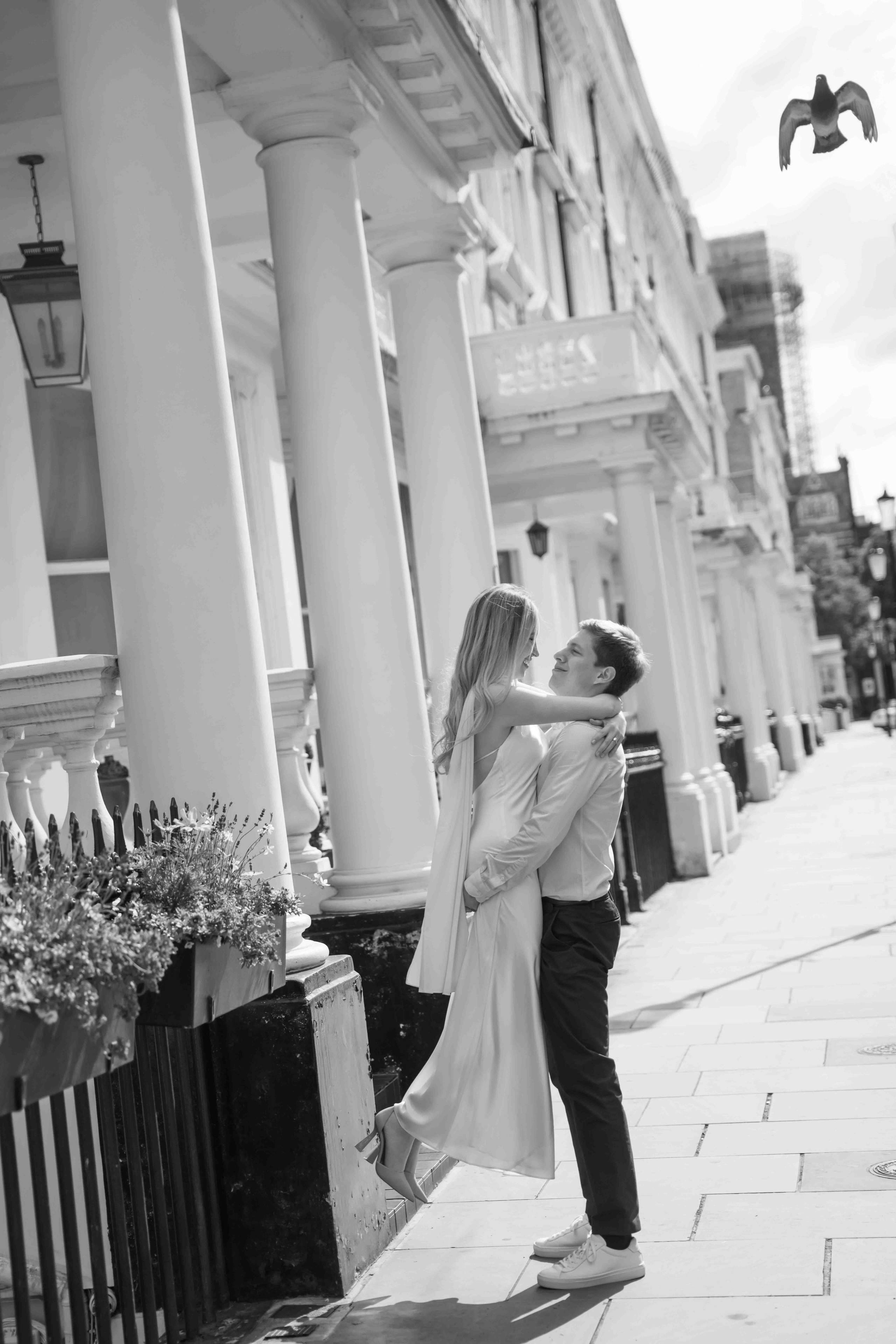 Black and white image of a man lifting a woman during a playful moment in a London engagement photoshoot