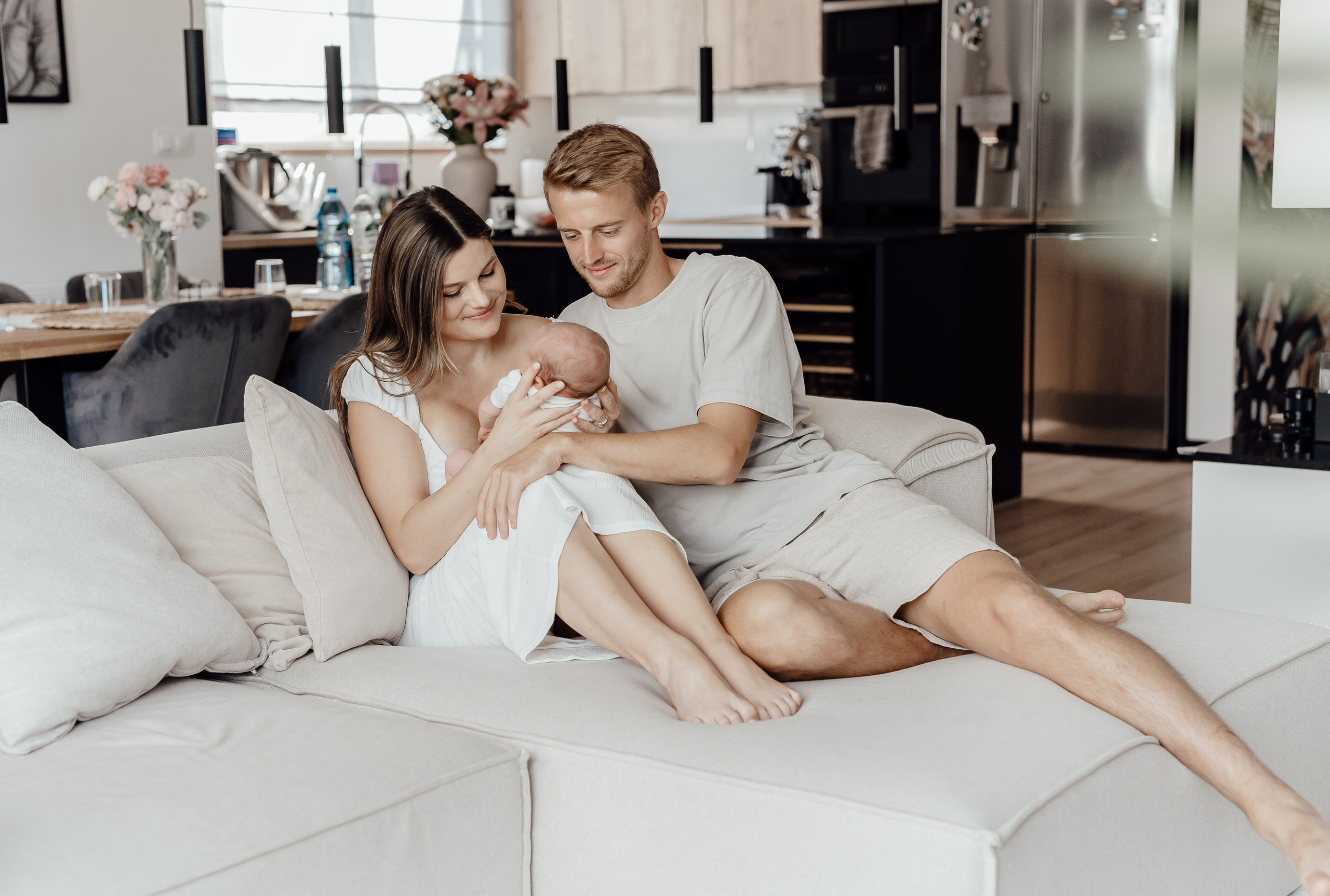 Rodzice całujący dziecko na łóżku – sesja noworodkowa w domu