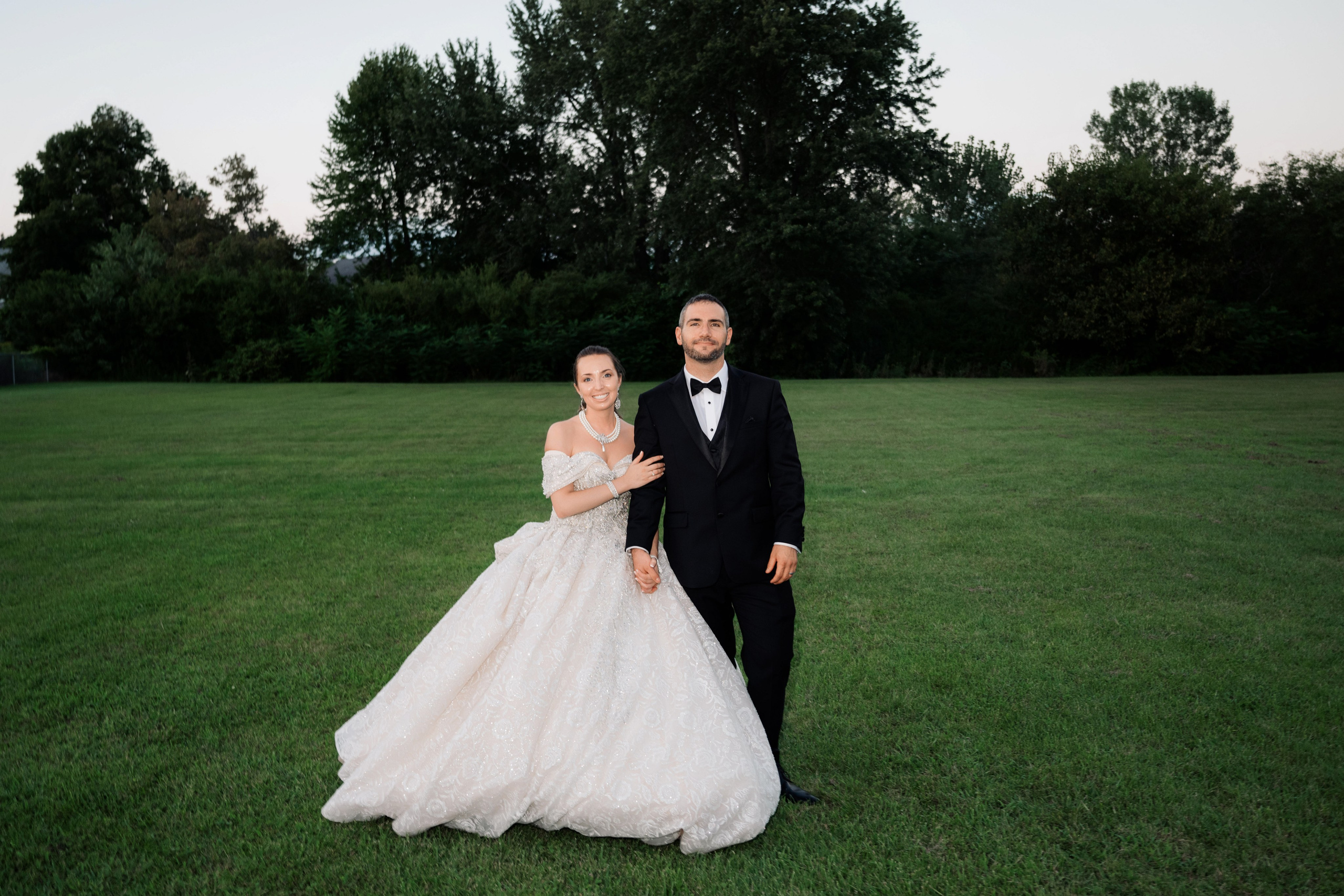 a bride and groom pose for a photo in a field