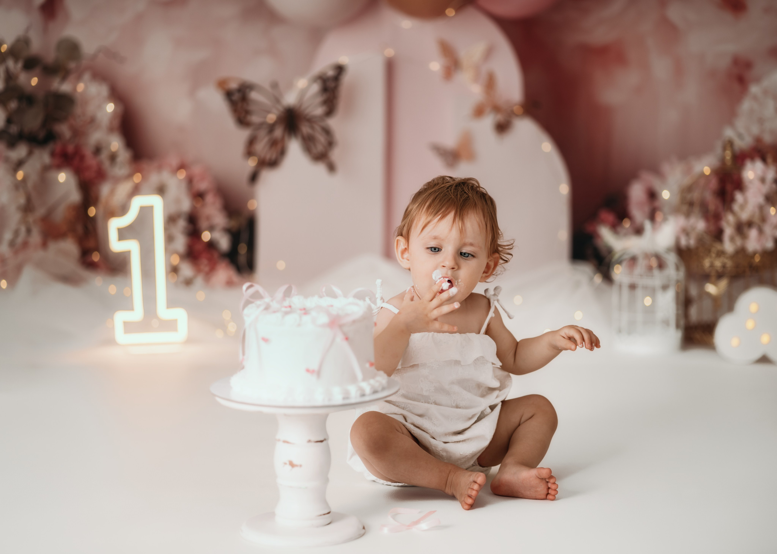 Prvi rođendan cake smash slikanje – beba u beloj haljinici u roze scenografiji sa balonima
