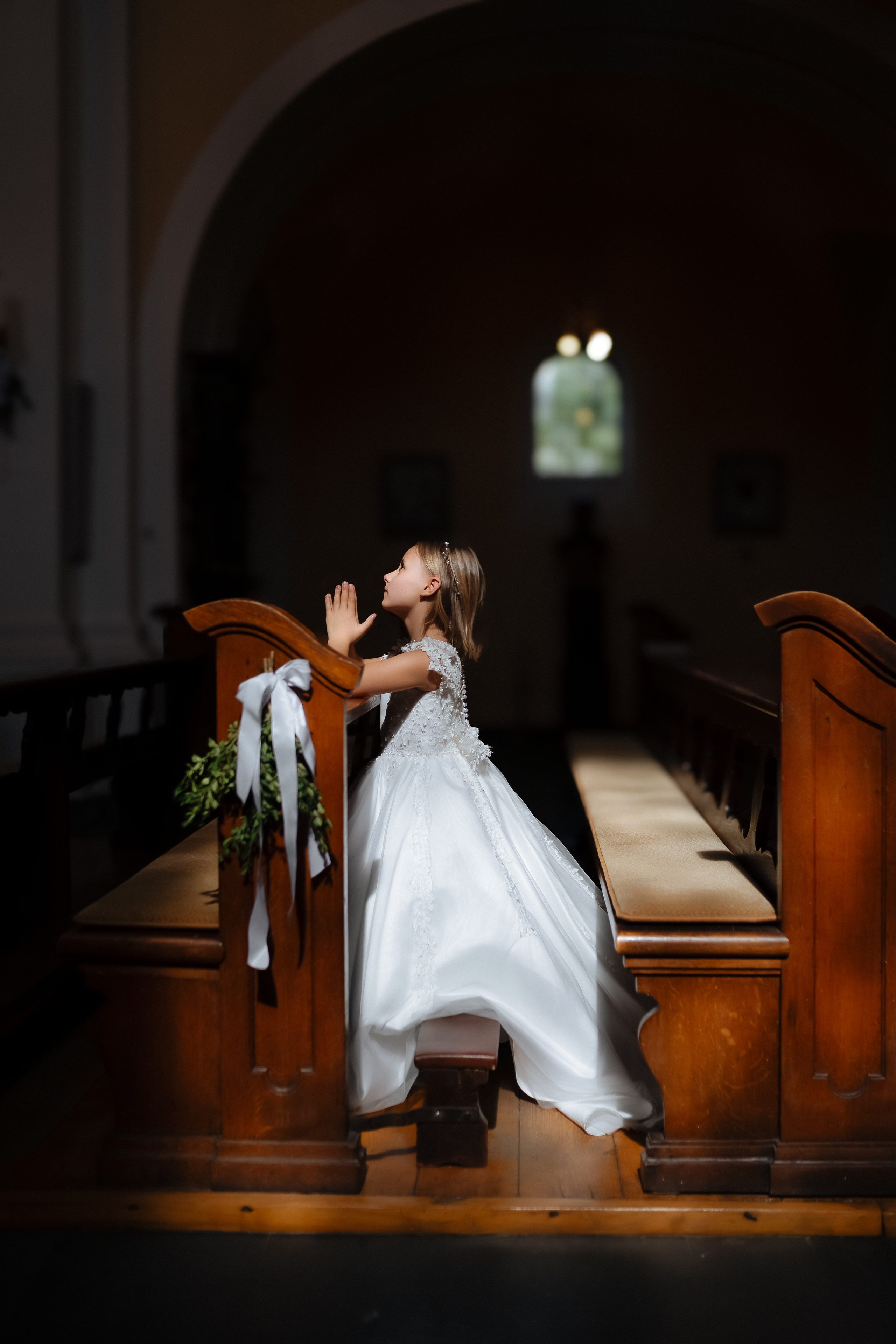 Mädchen in Kommunionkleid, das mit einer andächtigen Haltung im Gebet versunken ist. Fotoshooting Kommunion.