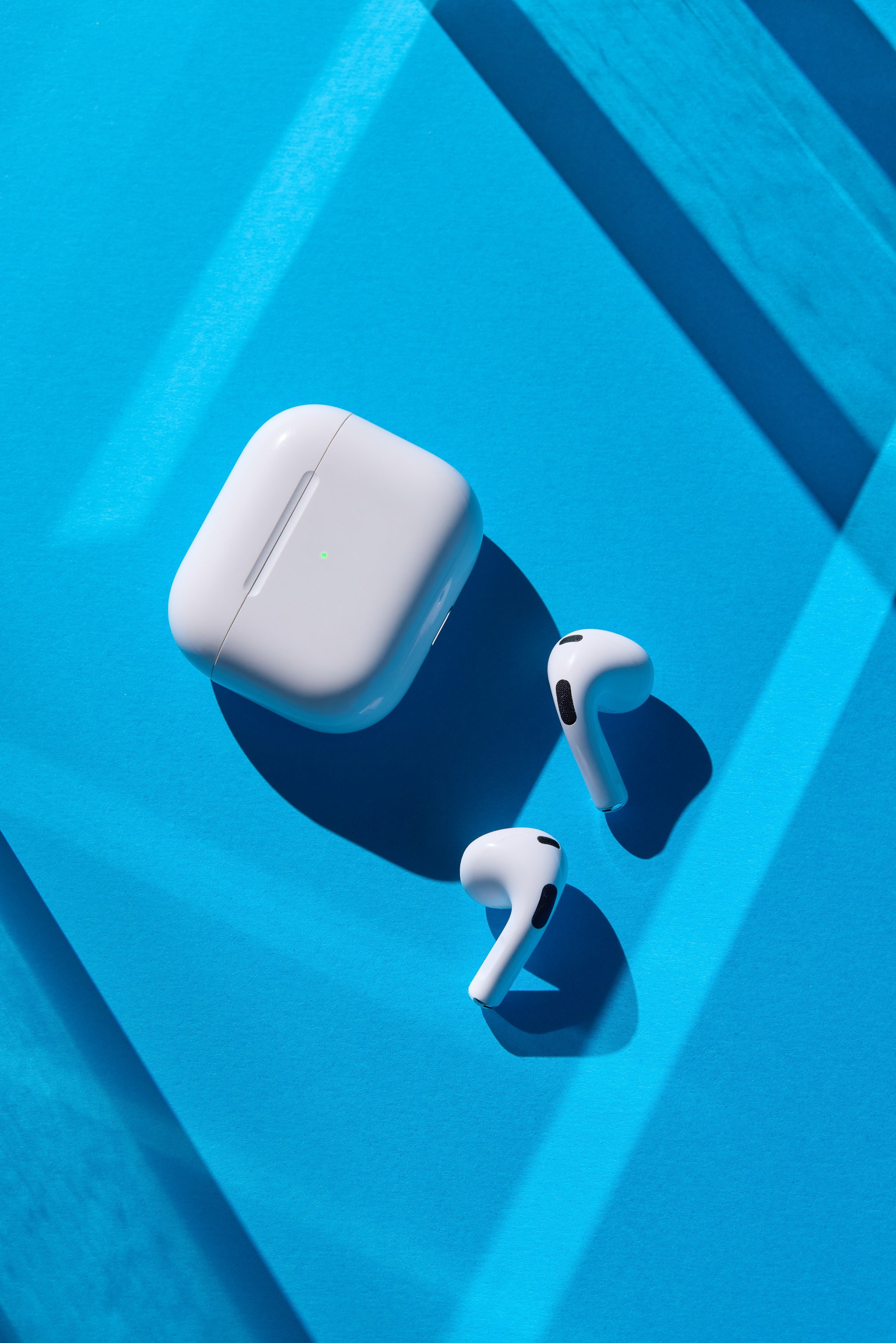 Apple AirPods на синем фоне с лучами света и контрастными тенями - фотограф Андрей Дунин