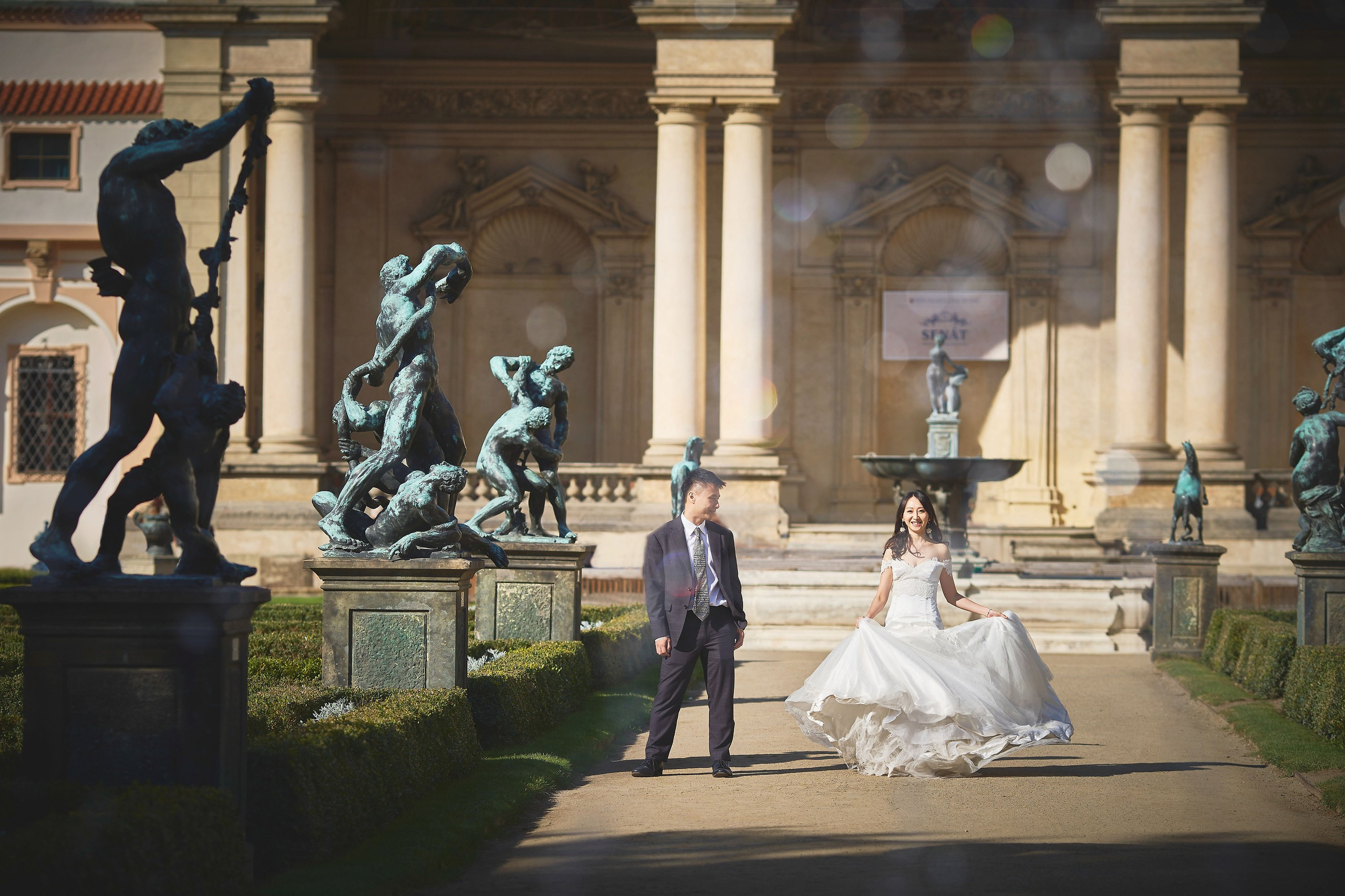 Bride Eva playfully spinning wedding dress near the statues in Wallenstein Garden.