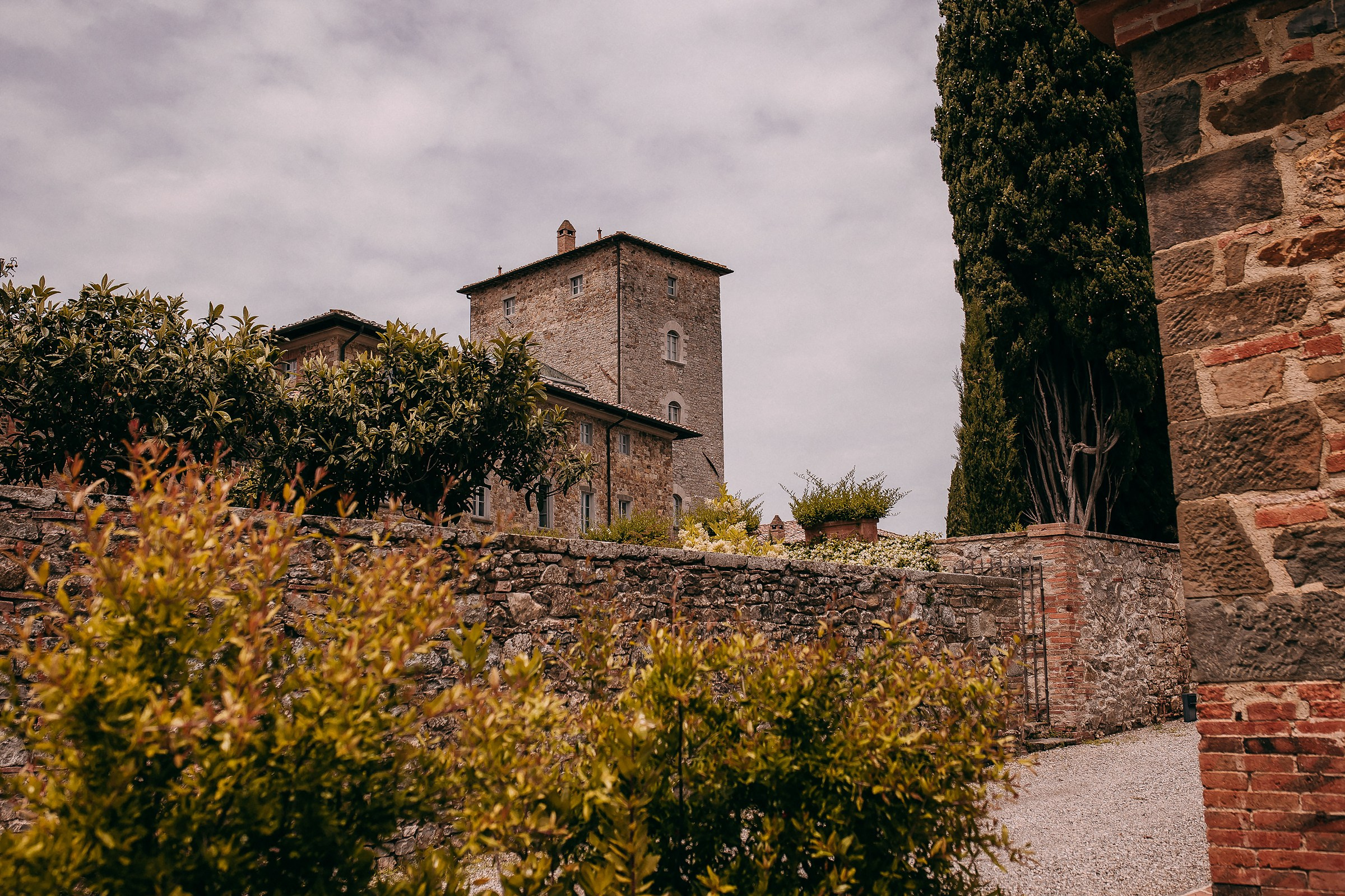 Rustic Borgo Scopeto in Tuscany, showcasing a historic stone tower surrounded by lush greenery under a partially cloudy sky.