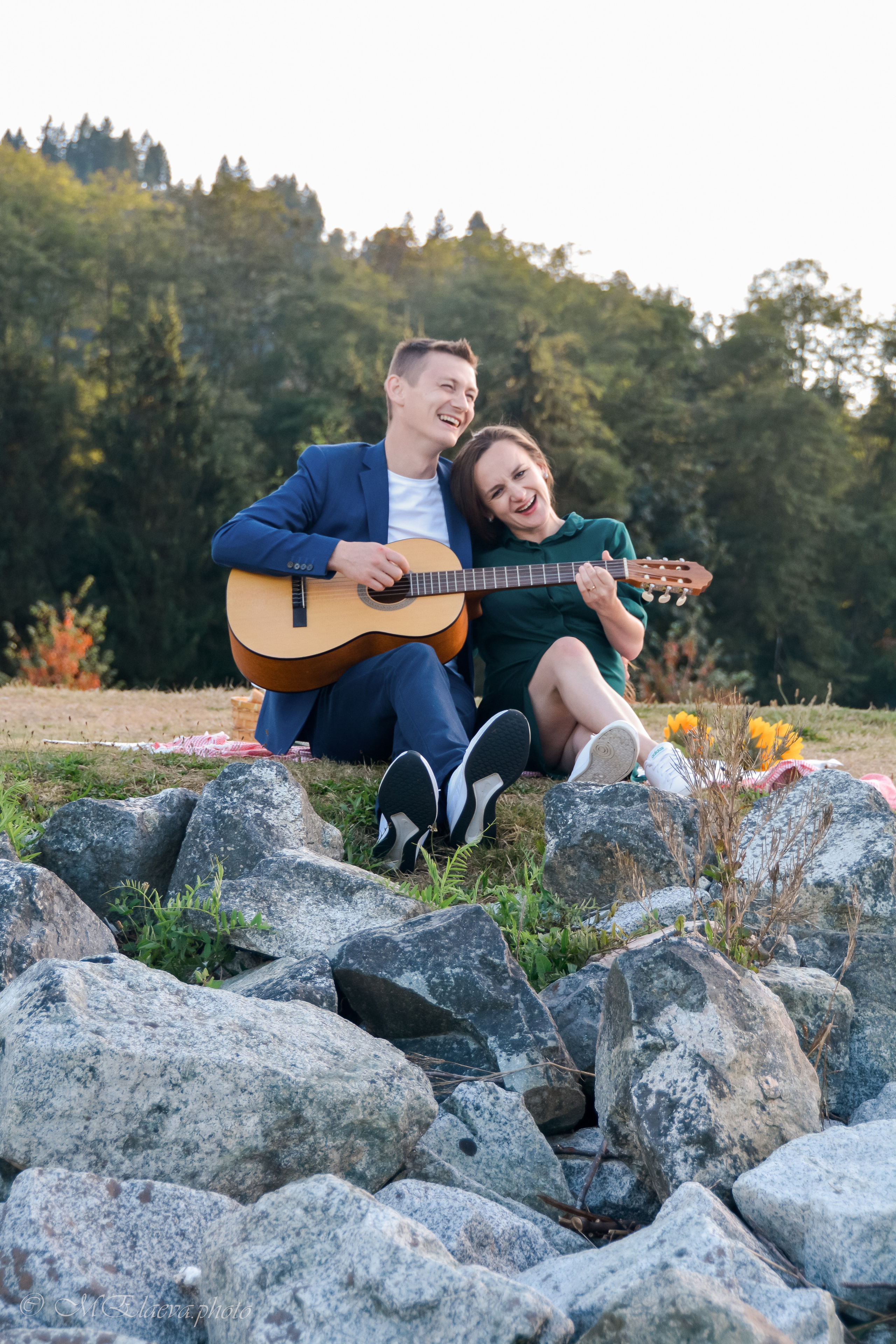 Candid moment of a couple sitting together on the shore in Burnaby, during golden hour, they are laughing, enjoying the moment