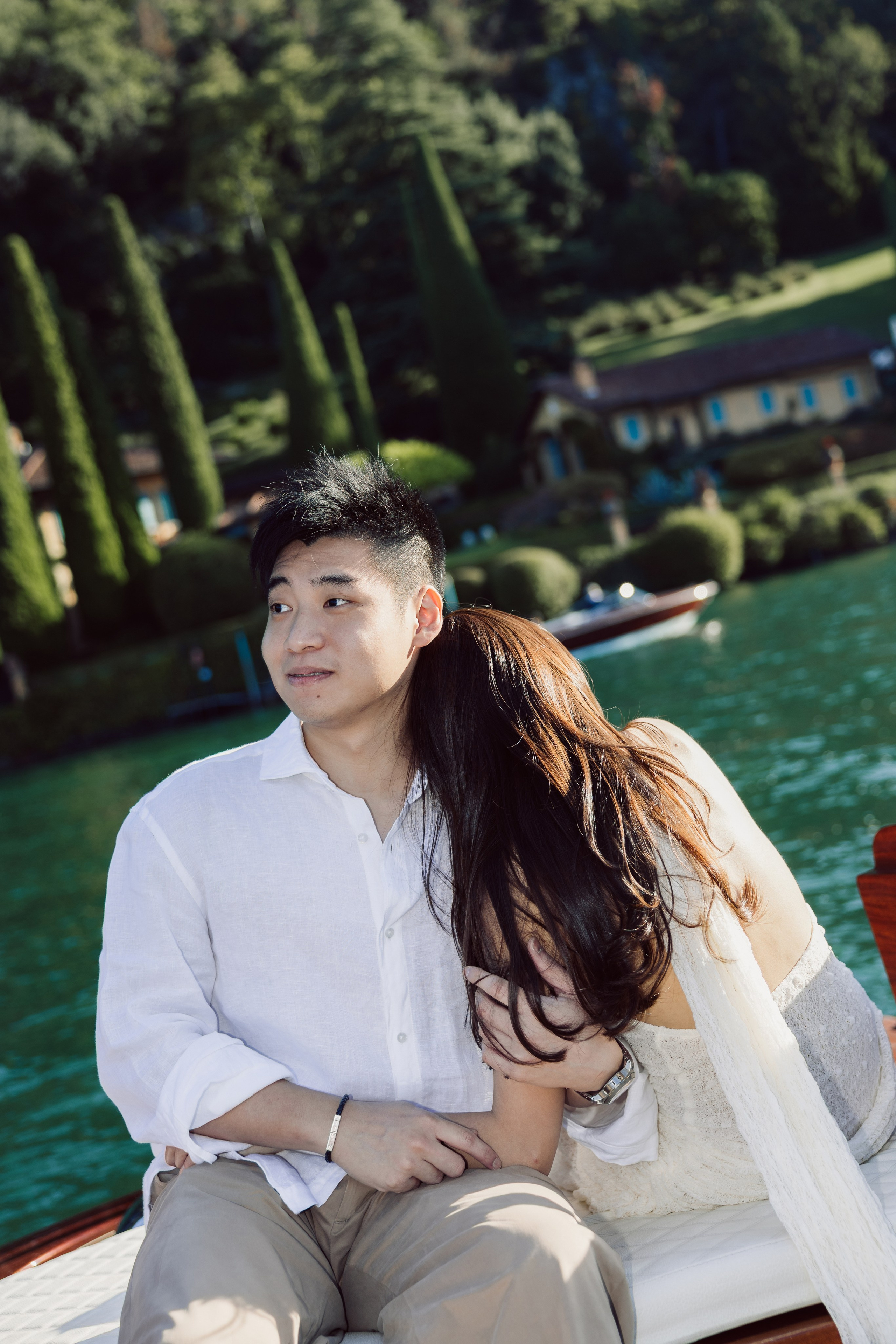 Couple sharing a quiet moment on a wooden boat near the lush green shoreline of Lake Como.