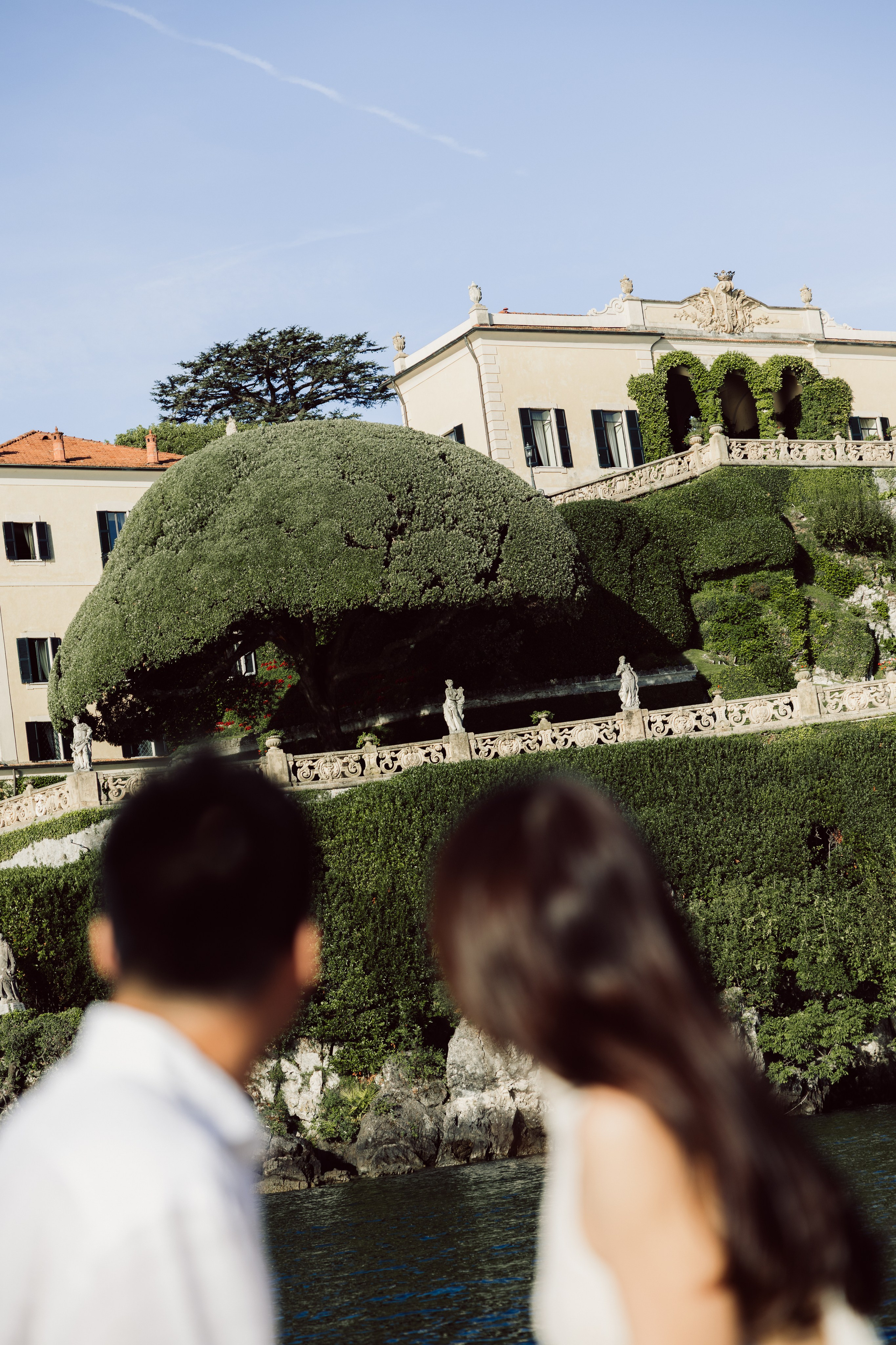 Couple admiring a historic lakeside Villa del Balbianello from their private boat on Lake Como