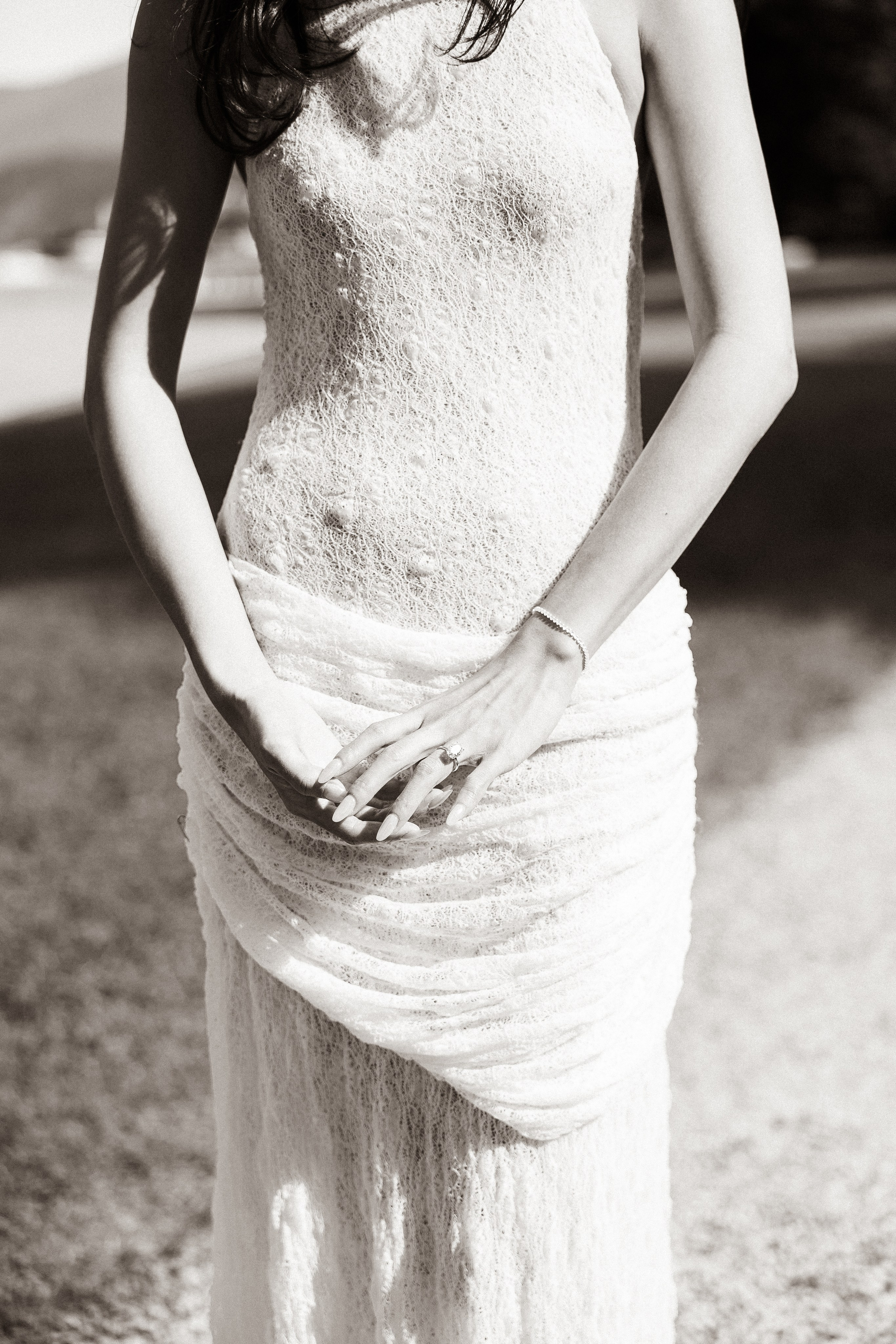 Black and white detail photograph of a woman's textured white dress and her hands gently clasped together.