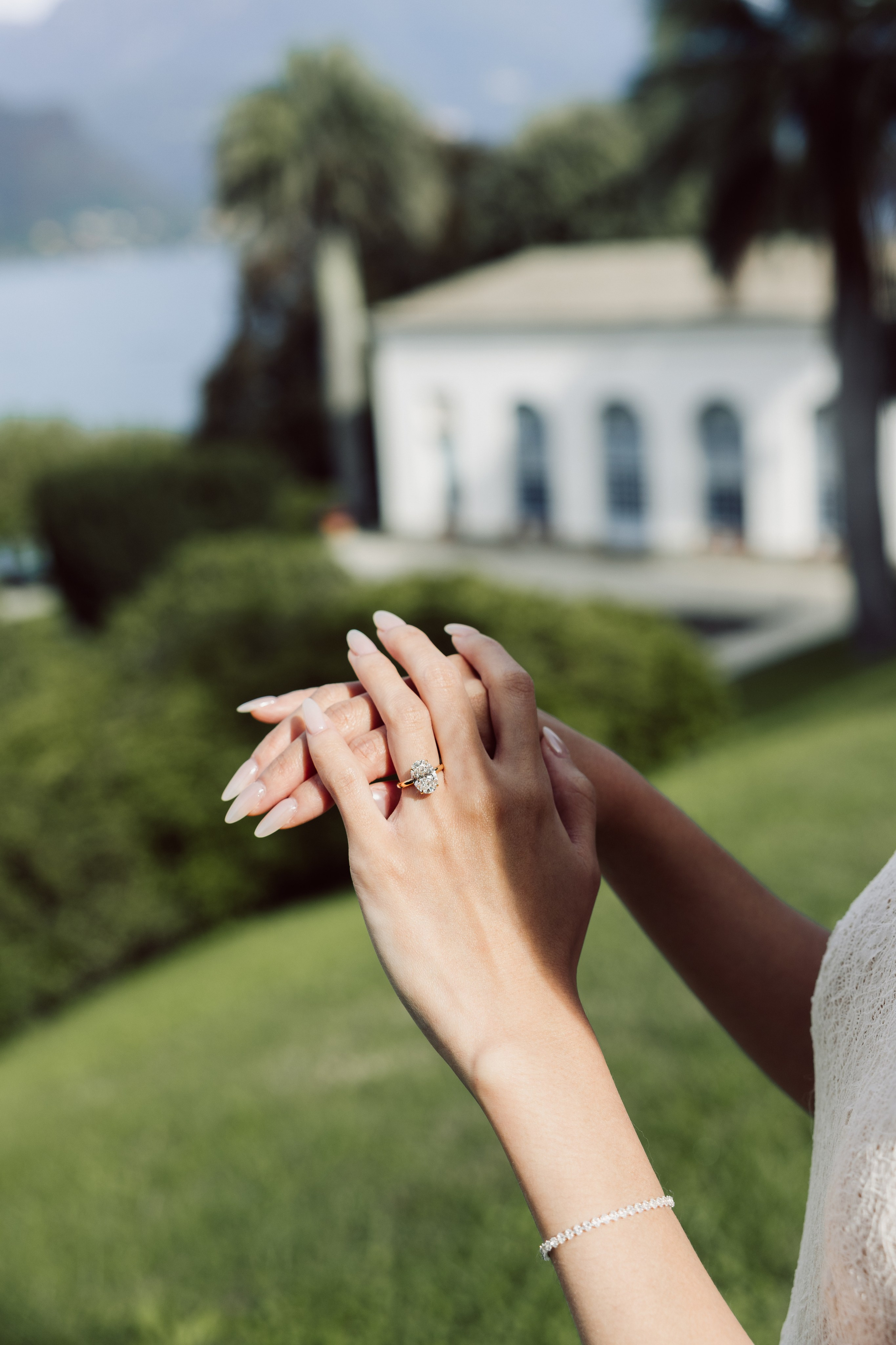 Close-up of an engagement ring on a woman's hand with the gardens of Villa Melzi softly blurred behind.