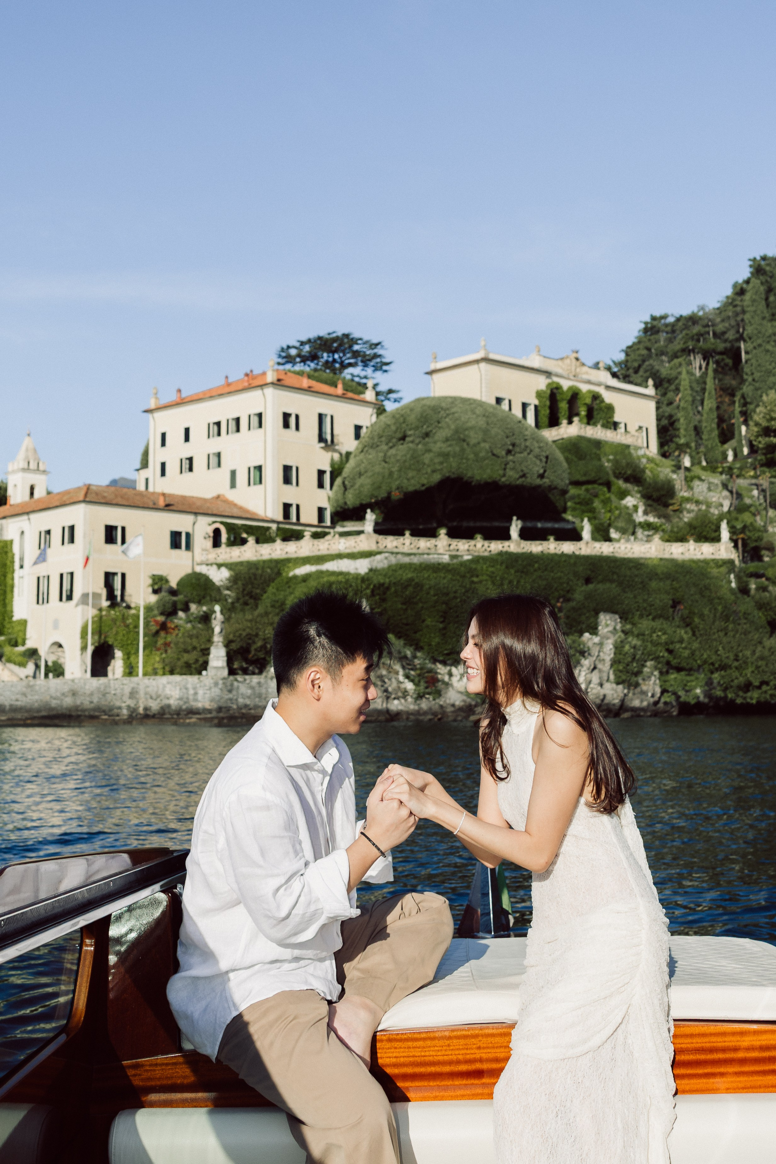 Couple kissing on a private boat with a beautiful lakeside Villa del Balbianello in the background