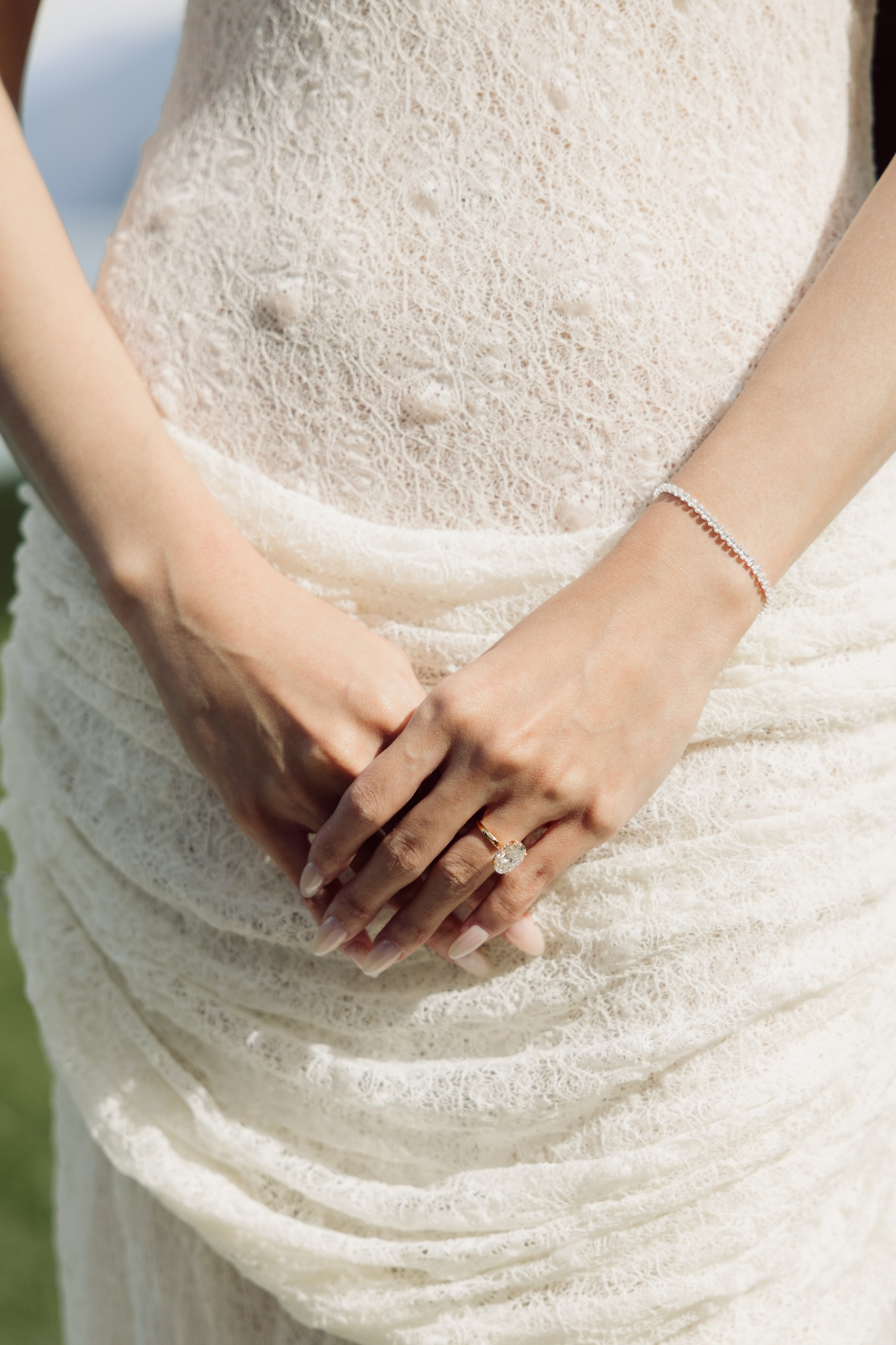 Close-up of an engagement ring on a woman's hands against an elegant white dress