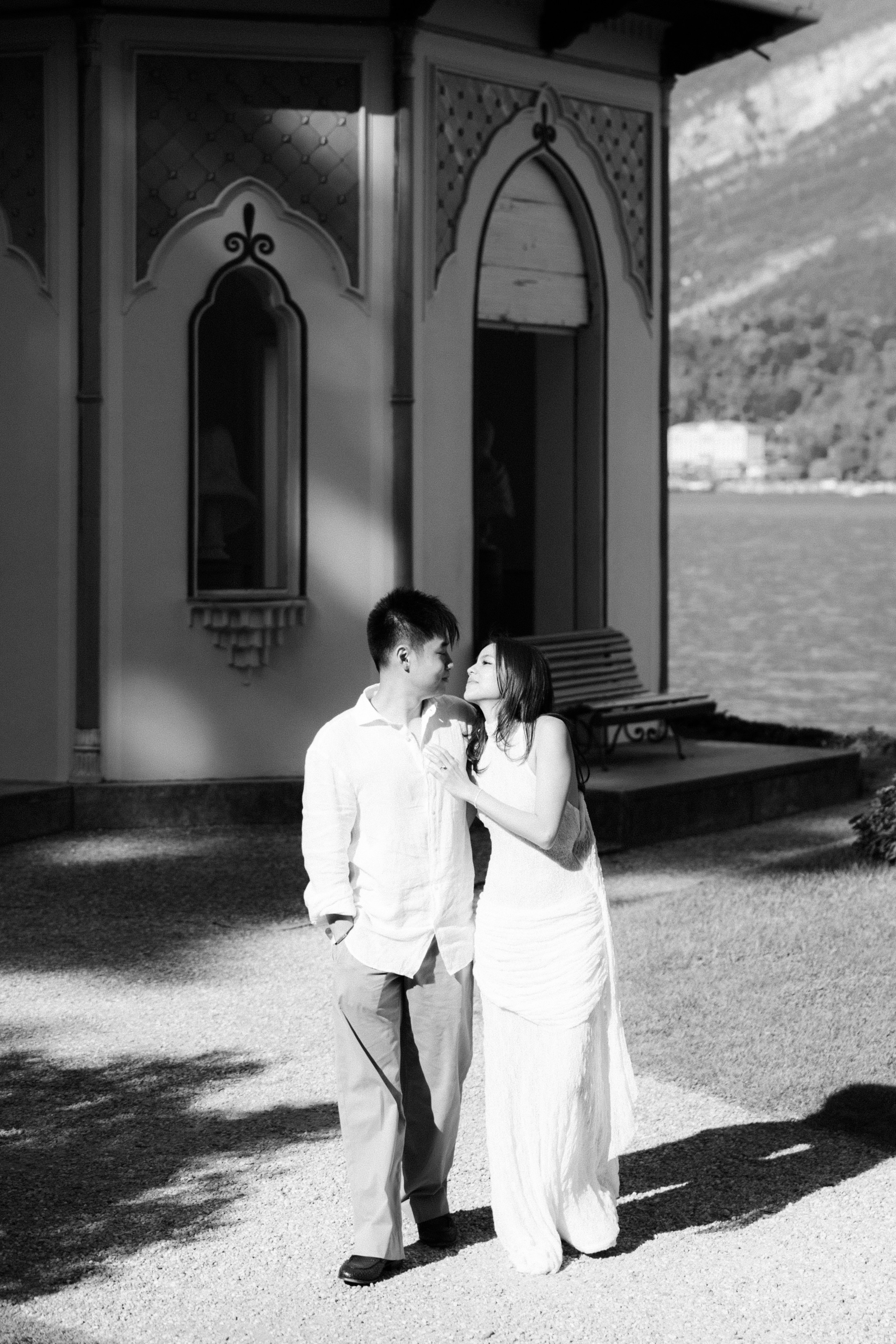 Black and white portrait of a couple smiling at each other beside a historic lakeside pavilion in Bellagio.