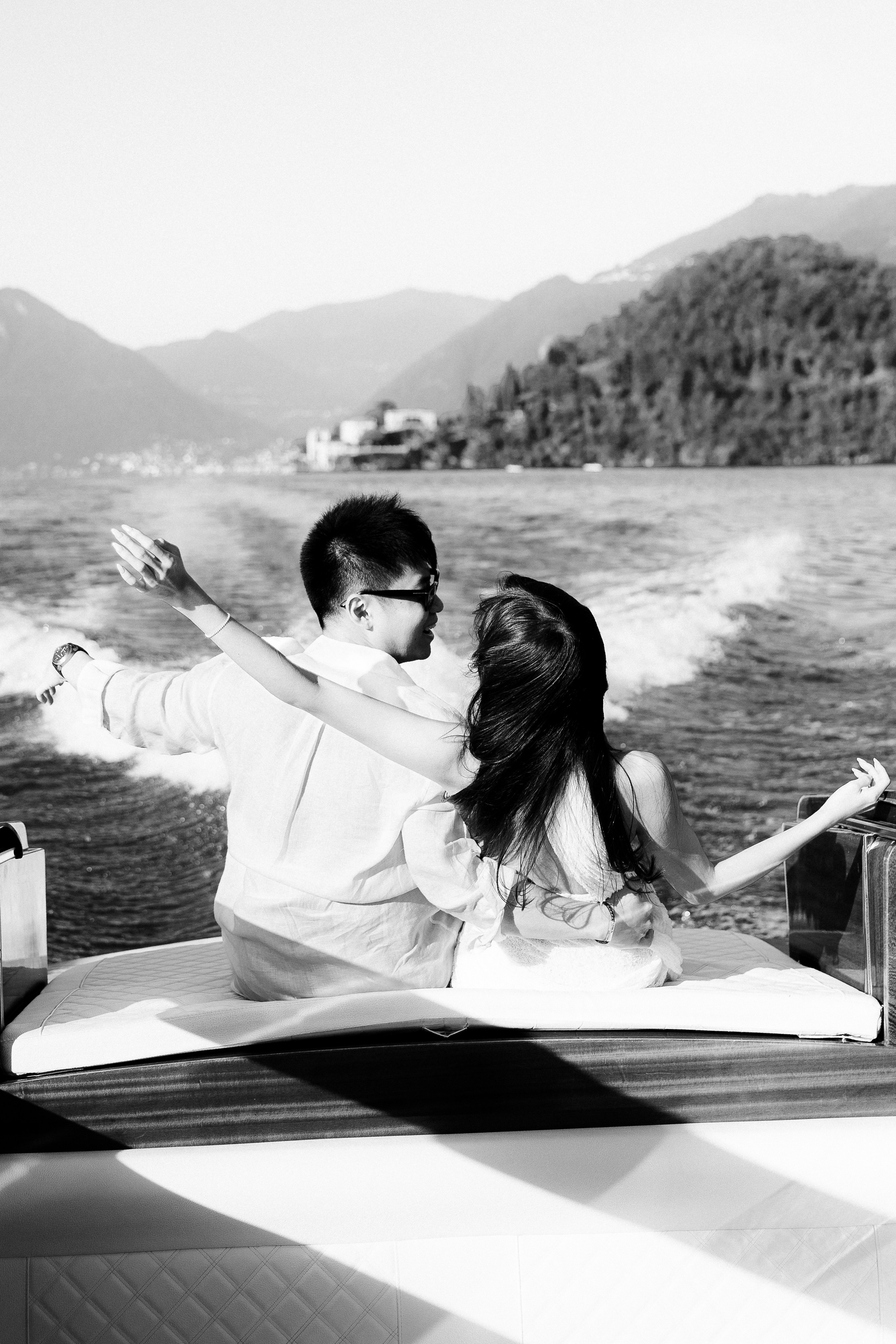 Black and white photograph of a couple enjoying a boat ride across Lake Como, seen from behind.
