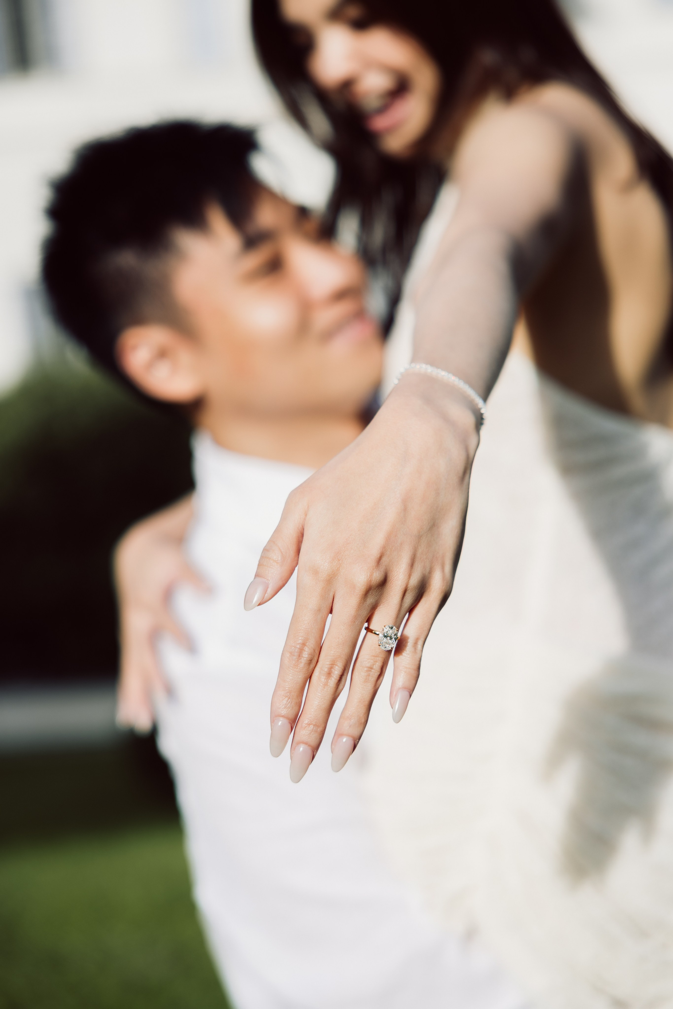 Close-up of a diamond engagement ring on a woman's hand as she embraces her partner in the gardens of Villa Melzi.