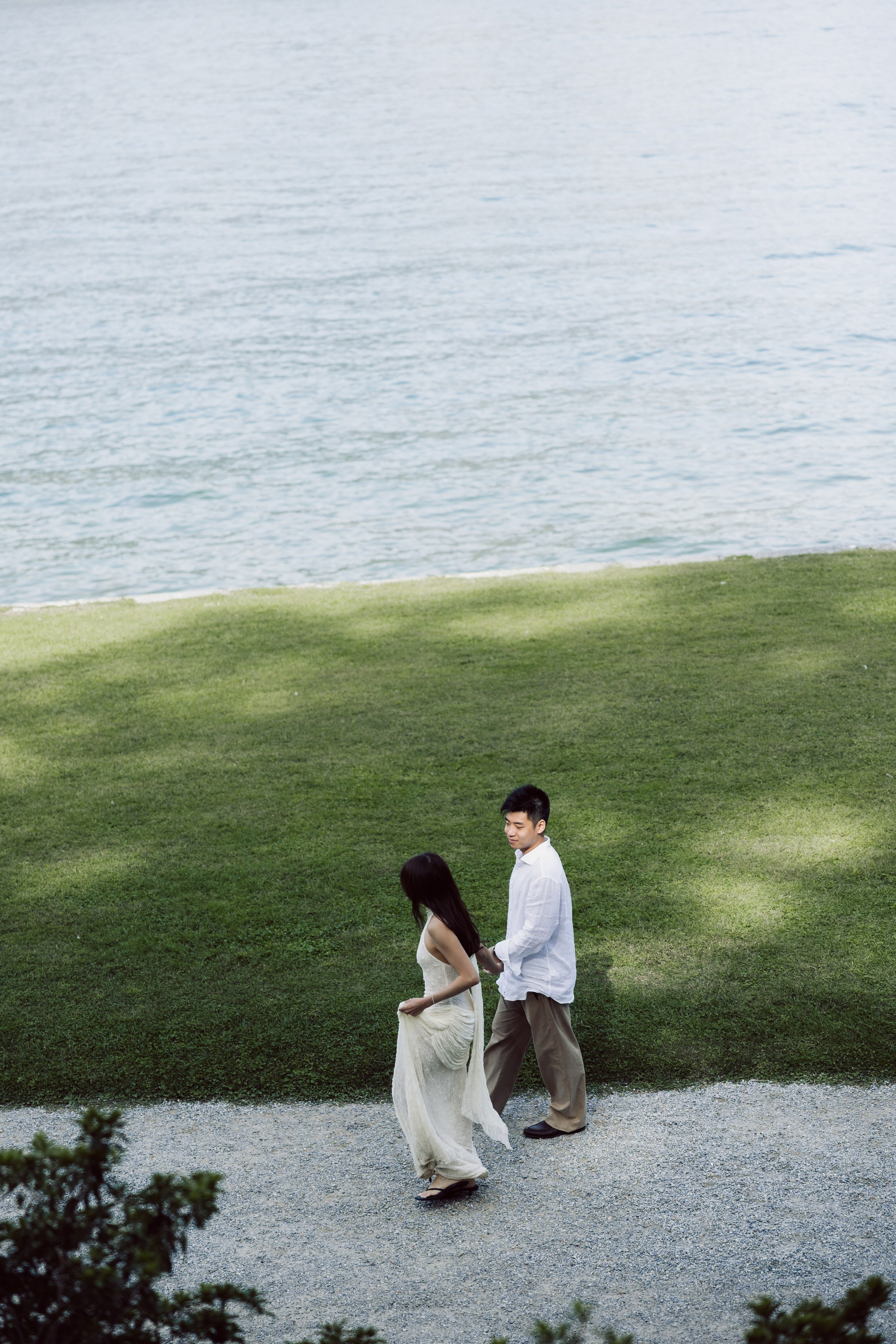 Couple walking along a gravel path beside the green lawns and waterfront of Villa Melzi, Lake Como.