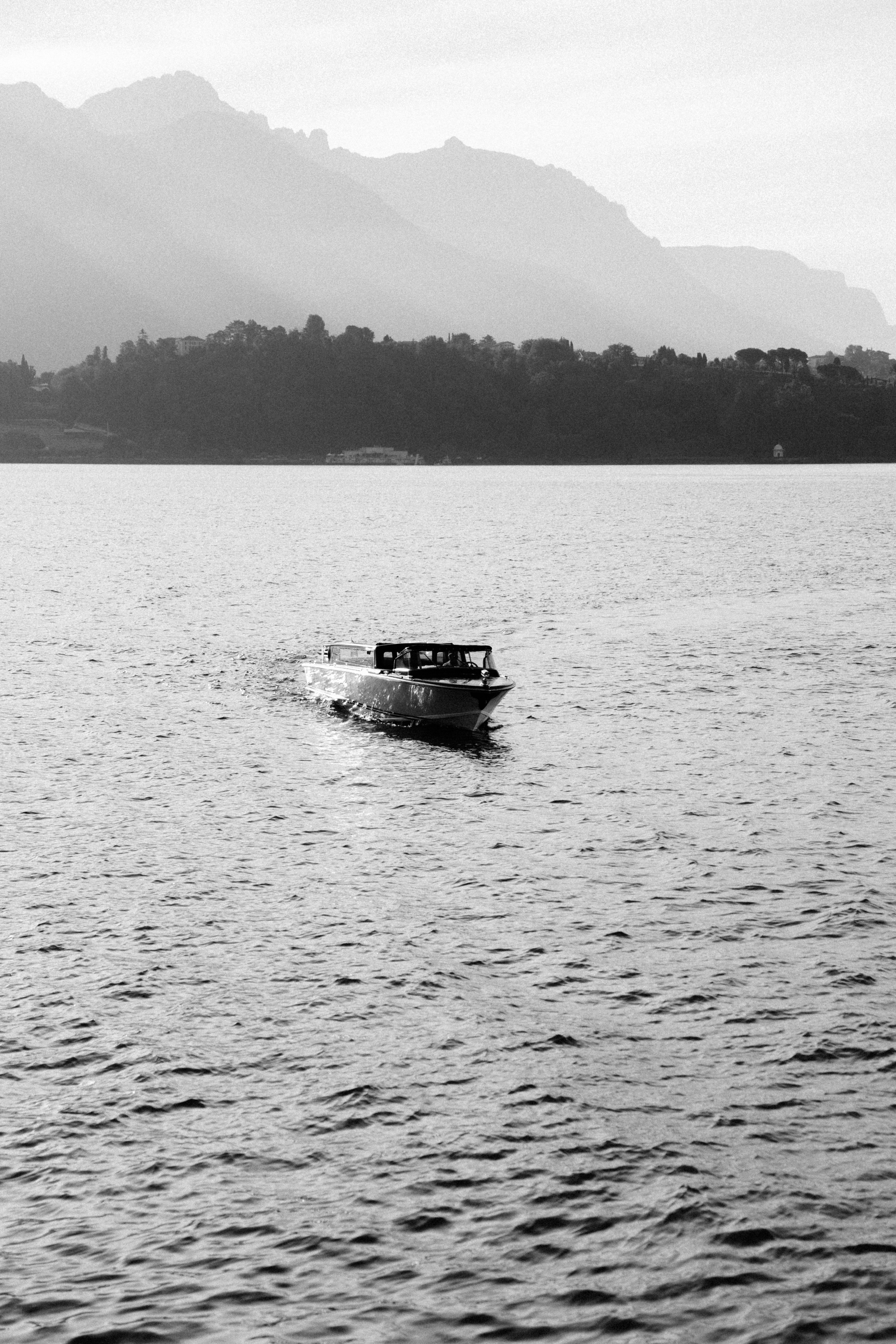 Black and white landscape of a motorboat cruising across Lake Como