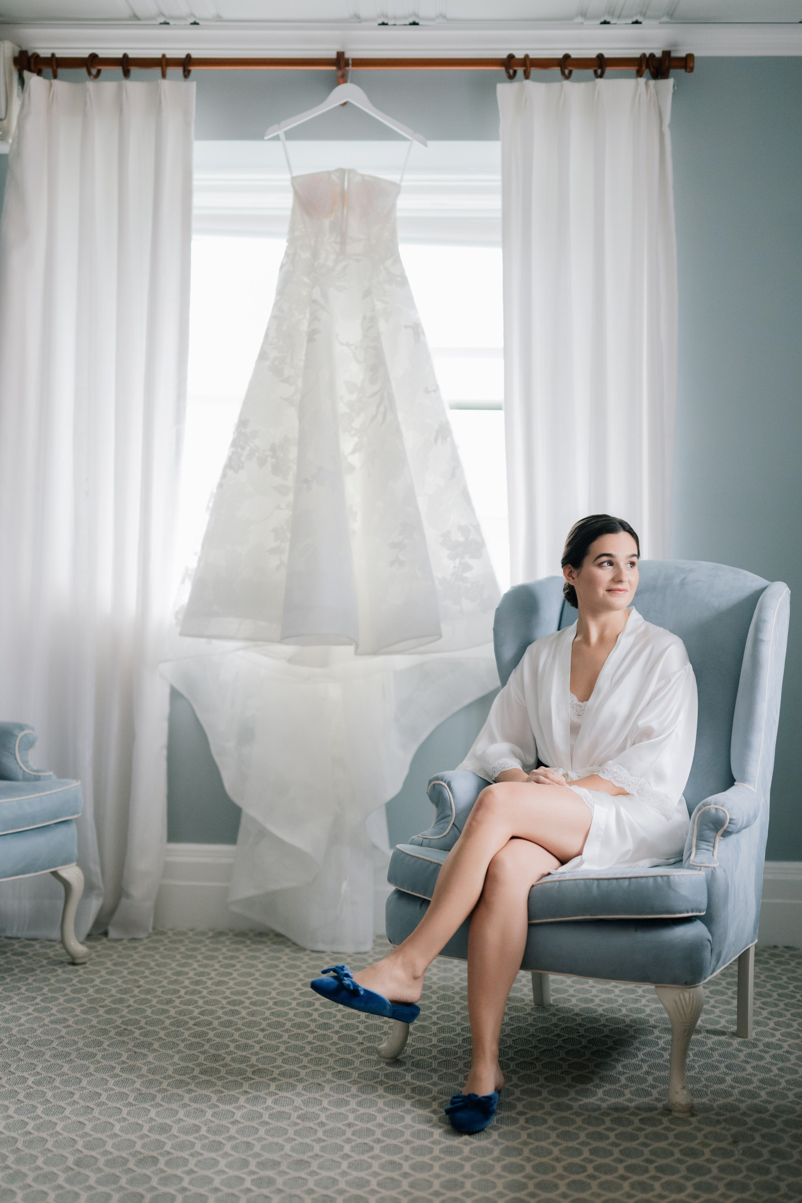 a woman sitting in a chair with a wedding dress hanging on the wall