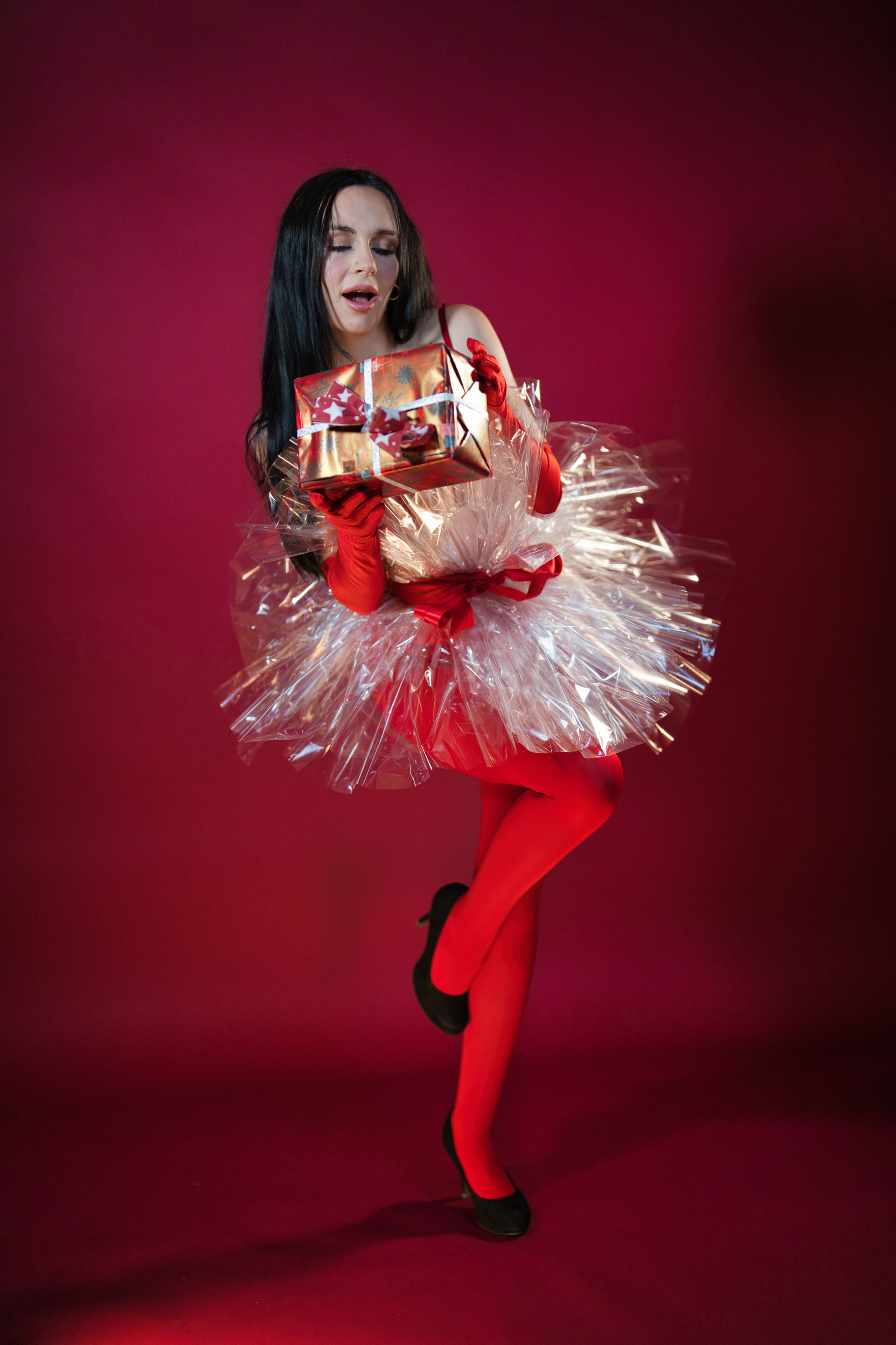 Frau sitzt neben Weihnachtsbaum auf rotem Hintergrund.