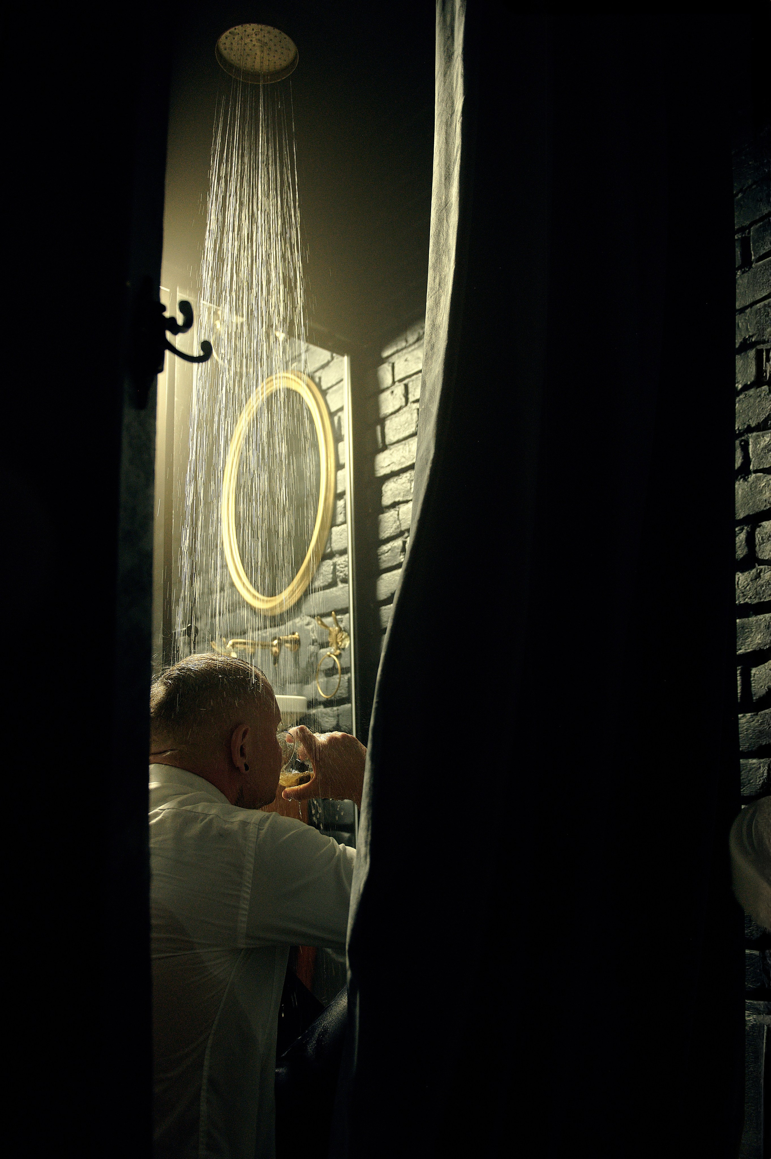 Deszcz z prysznica pada na mężczyznę w koszuli, który siedzi z drinkiem